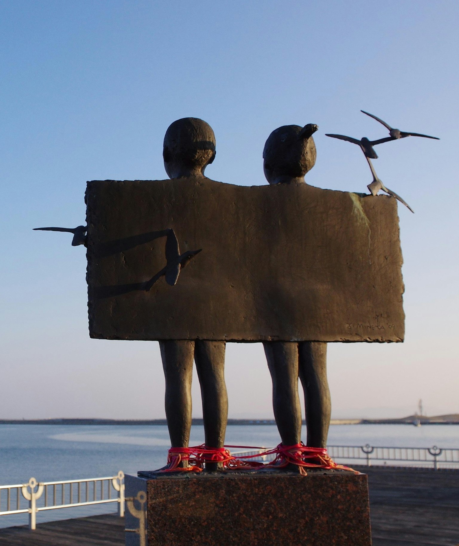 Escultura de dos niños mirando al mar con aves volando alrededor