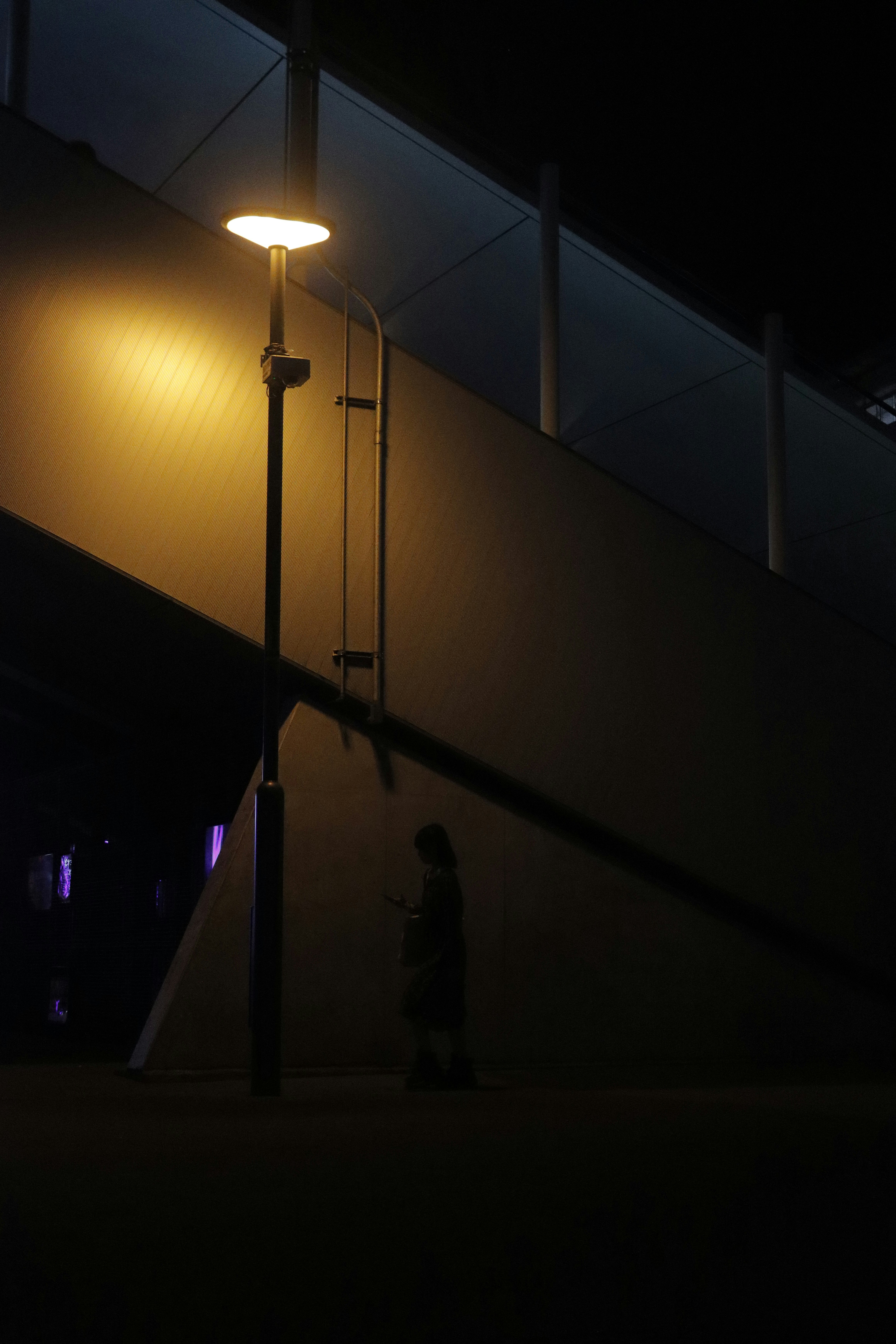 silhouetted figure standing along a wall under streetlights at night