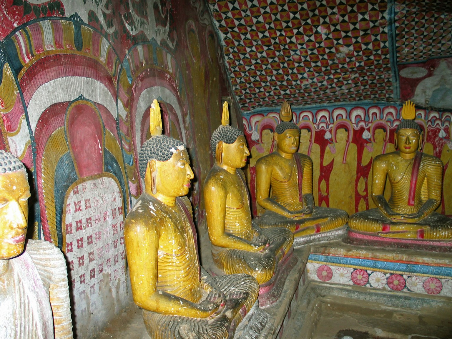 Golden Buddha statues in a Buddhist cave temple with vibrant wall paintings
