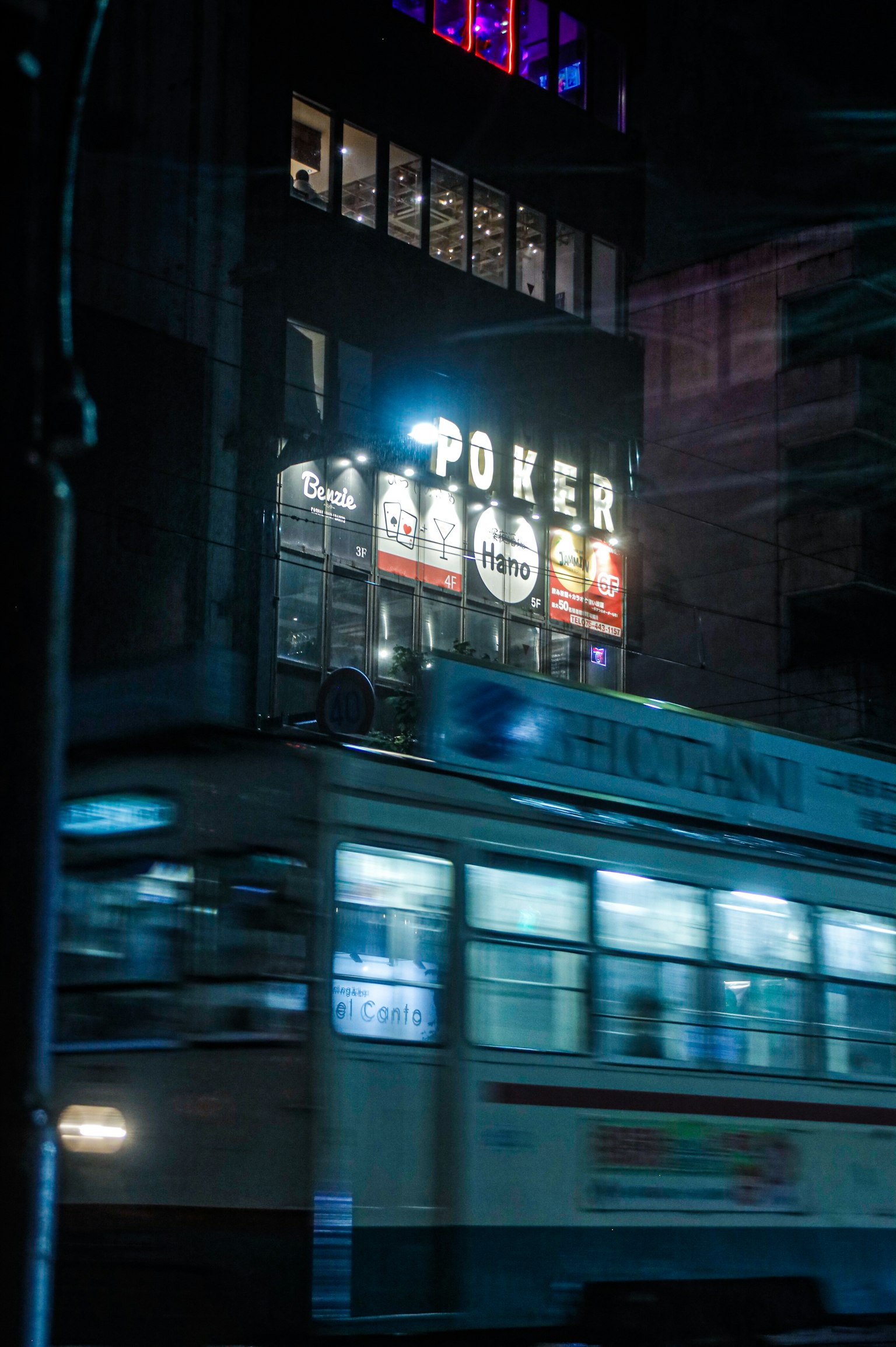 夜の街の中で動くトラムとポーカーの看板が映る