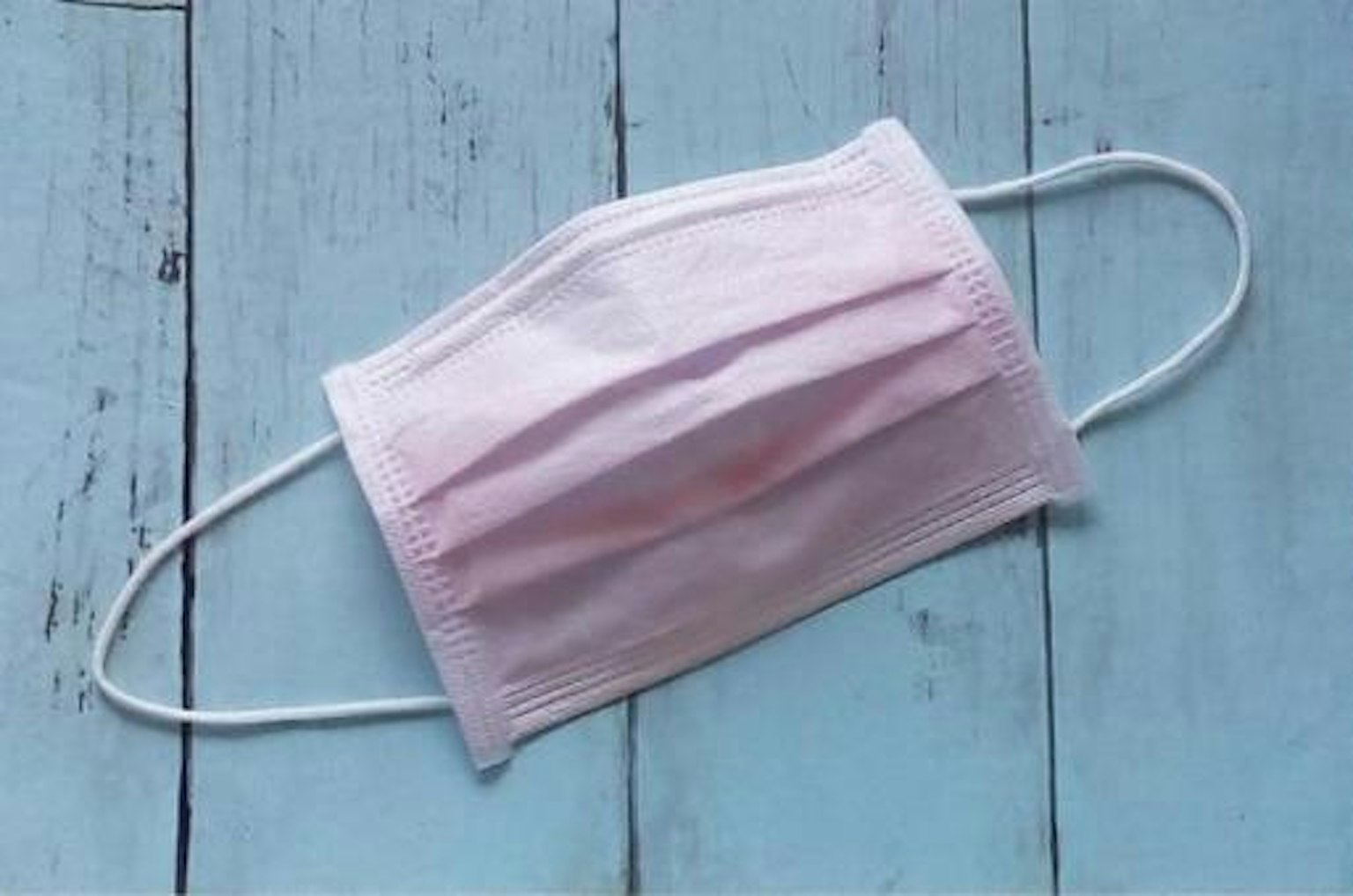 Masker pink muda diletakkan di atas latar belakang kayu biru
