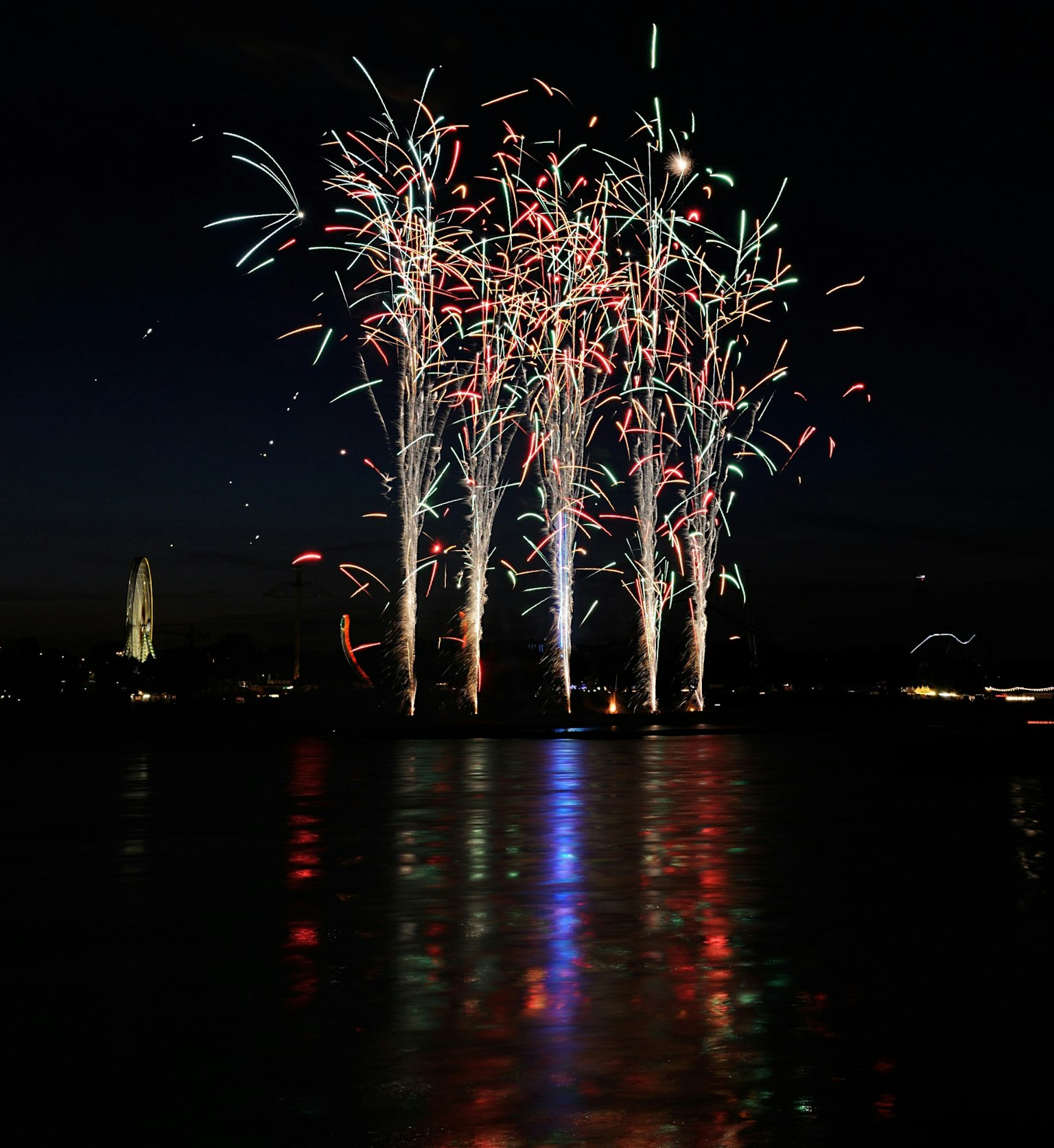 Spectacle de feux d'artifice colorés au-dessus de l'eau la nuit se reflétant à la surface
