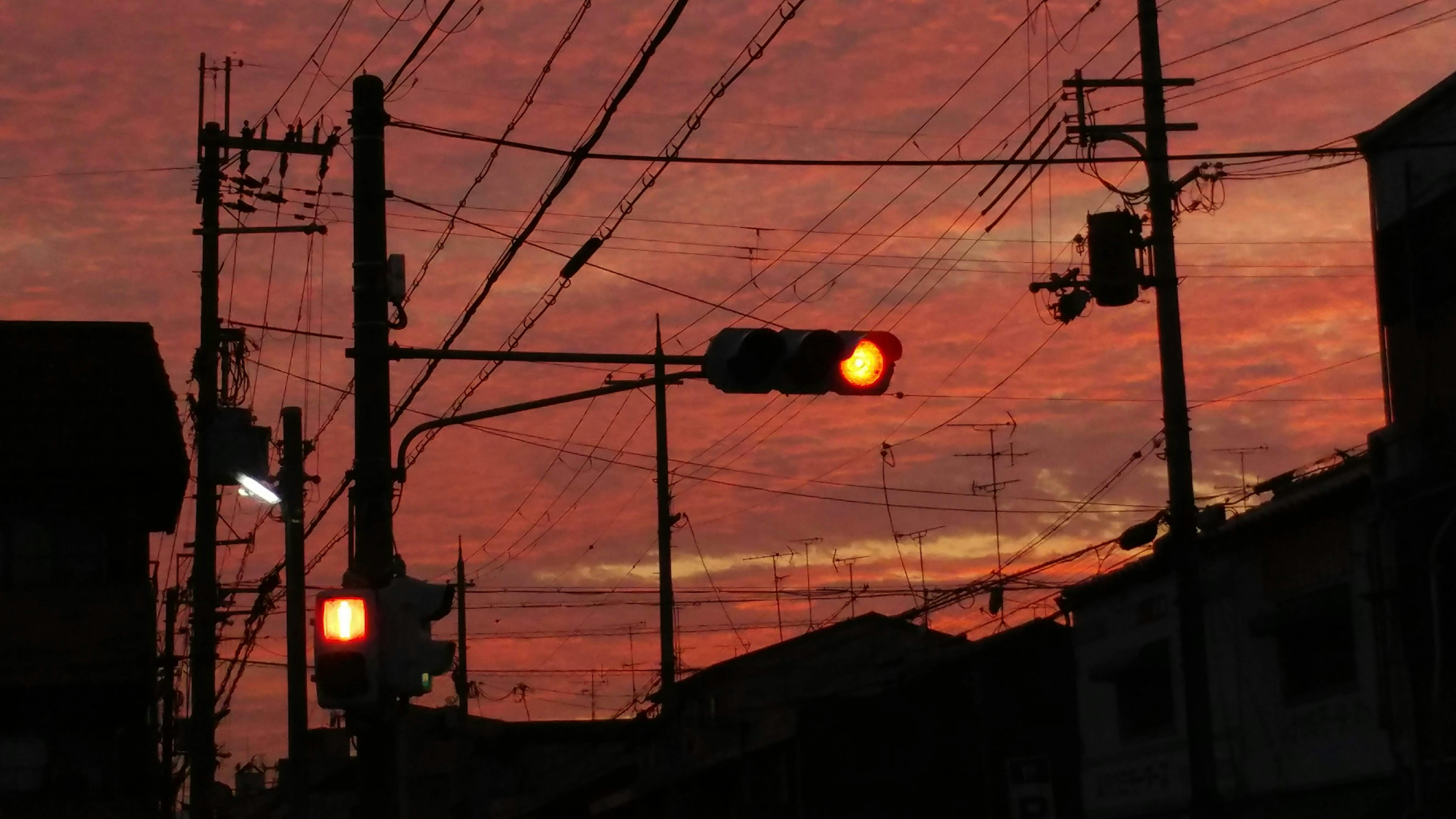 夕焼けの空に信号機と電線が走る路地