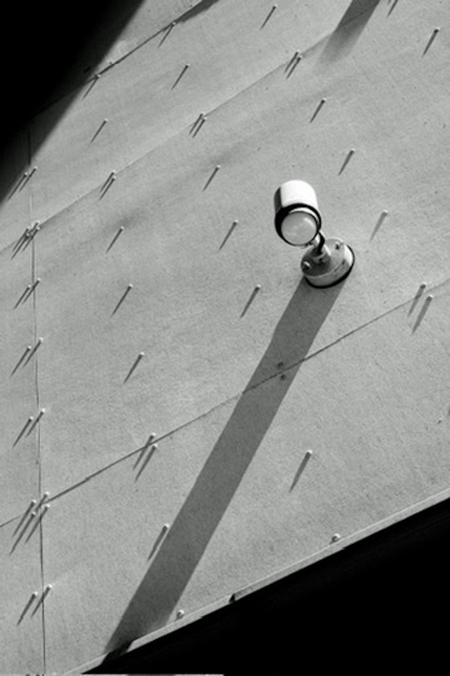 Projecteur fixé à un mur métallique projetant une longue ombre