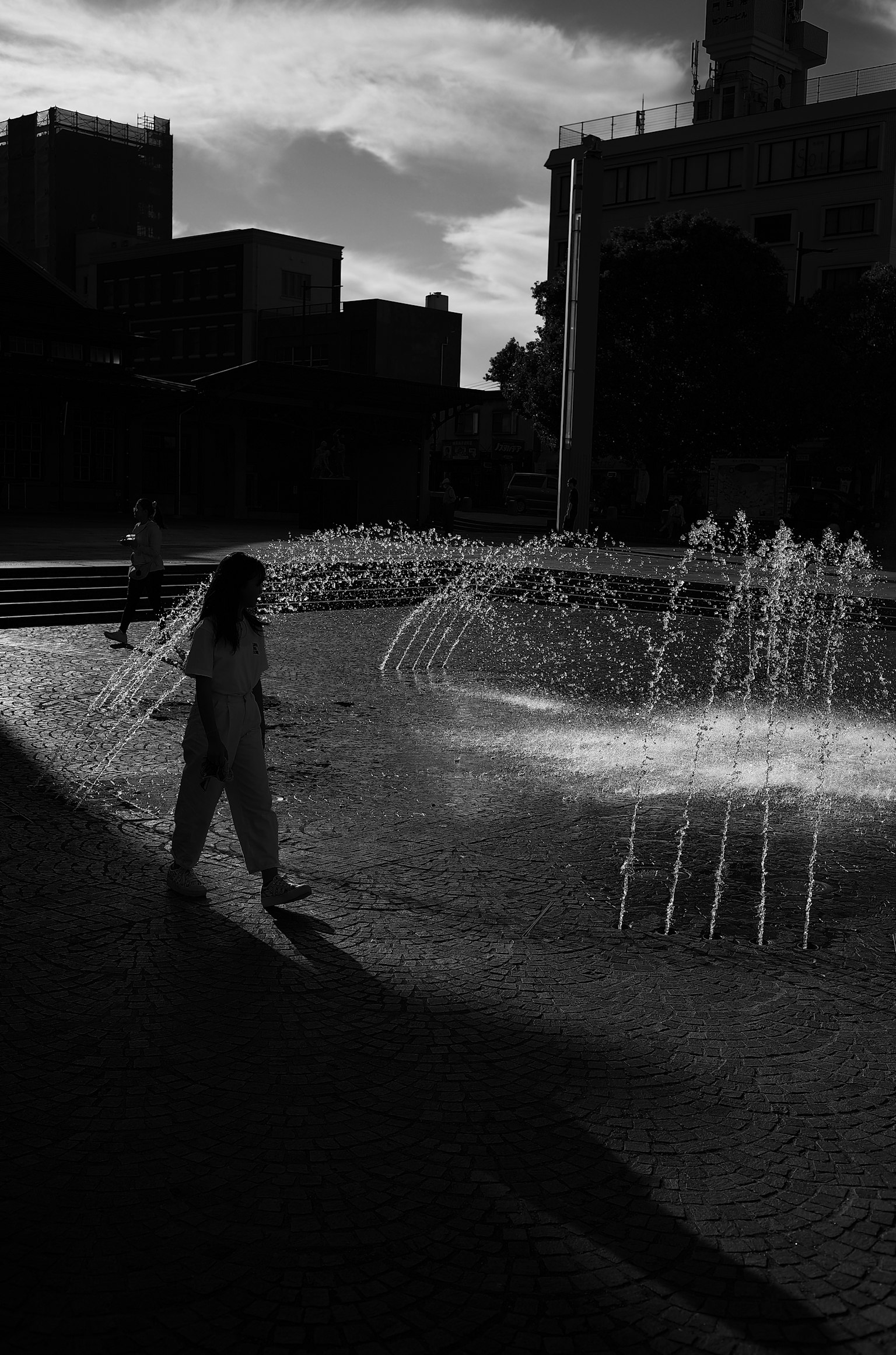 Donna che cammina davanti a una fontana in bianco e nero con ombre