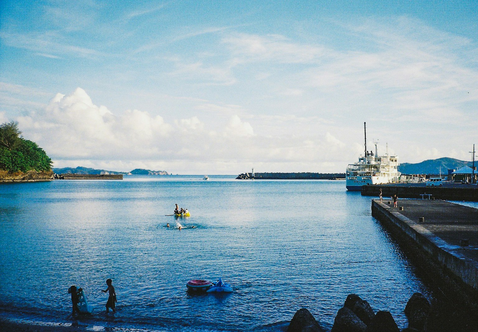 Calm sea and blue sky scene Boat docked at the harbor with people playing at the beach