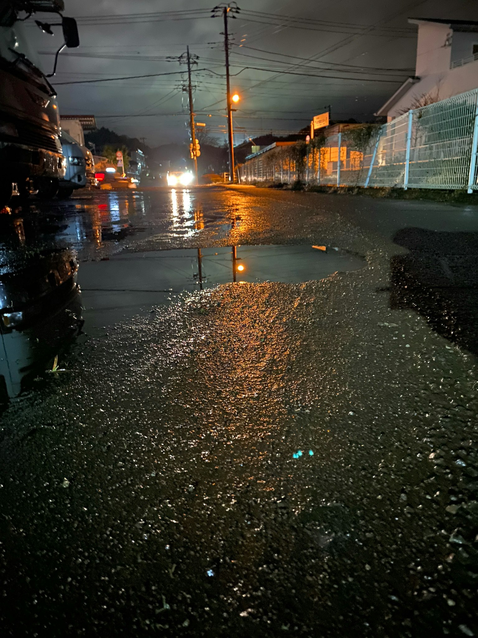 Street at night with puddles reflecting lights and dark clouds