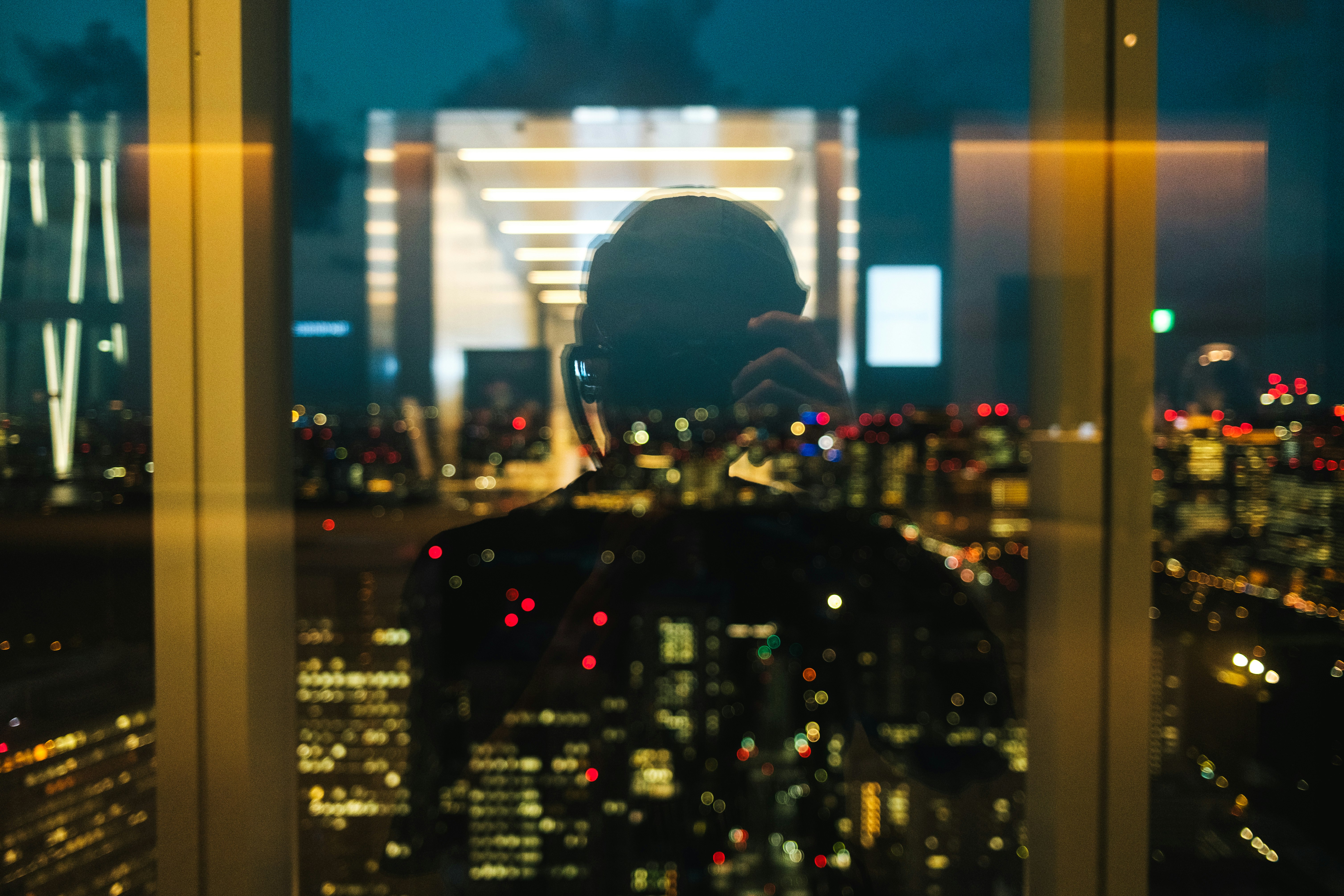 夜景を背景に窓越しでスマホを見つめる人物