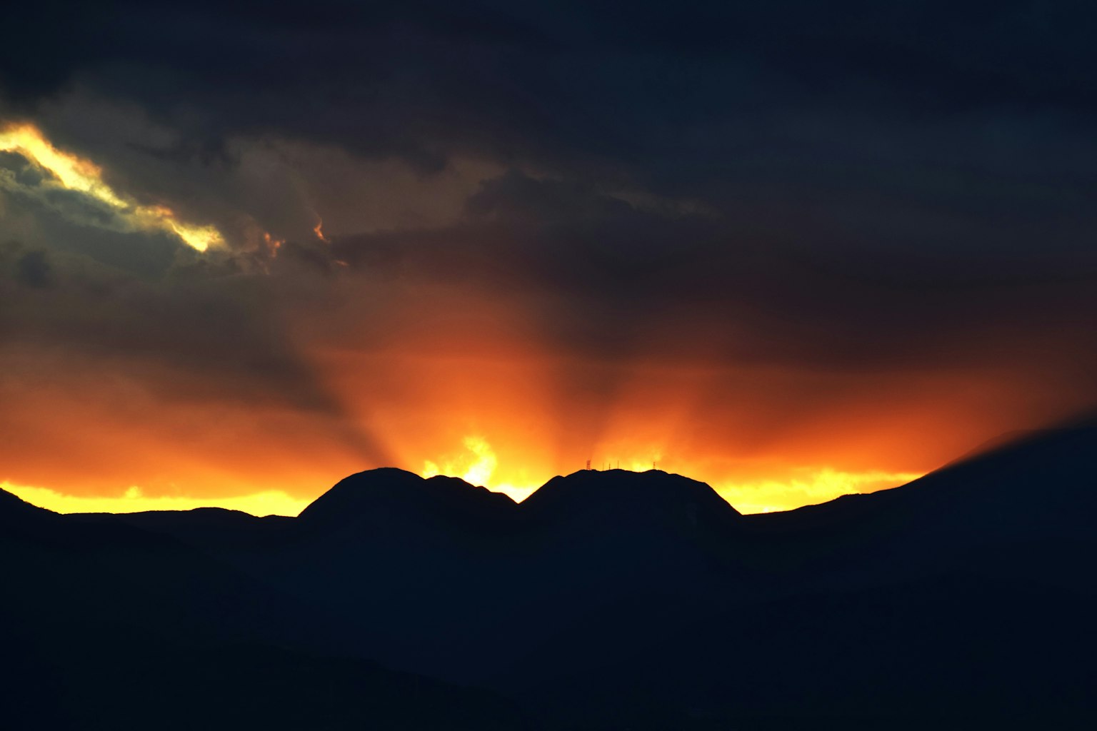 Orange sun rising between mountains with dark clouds