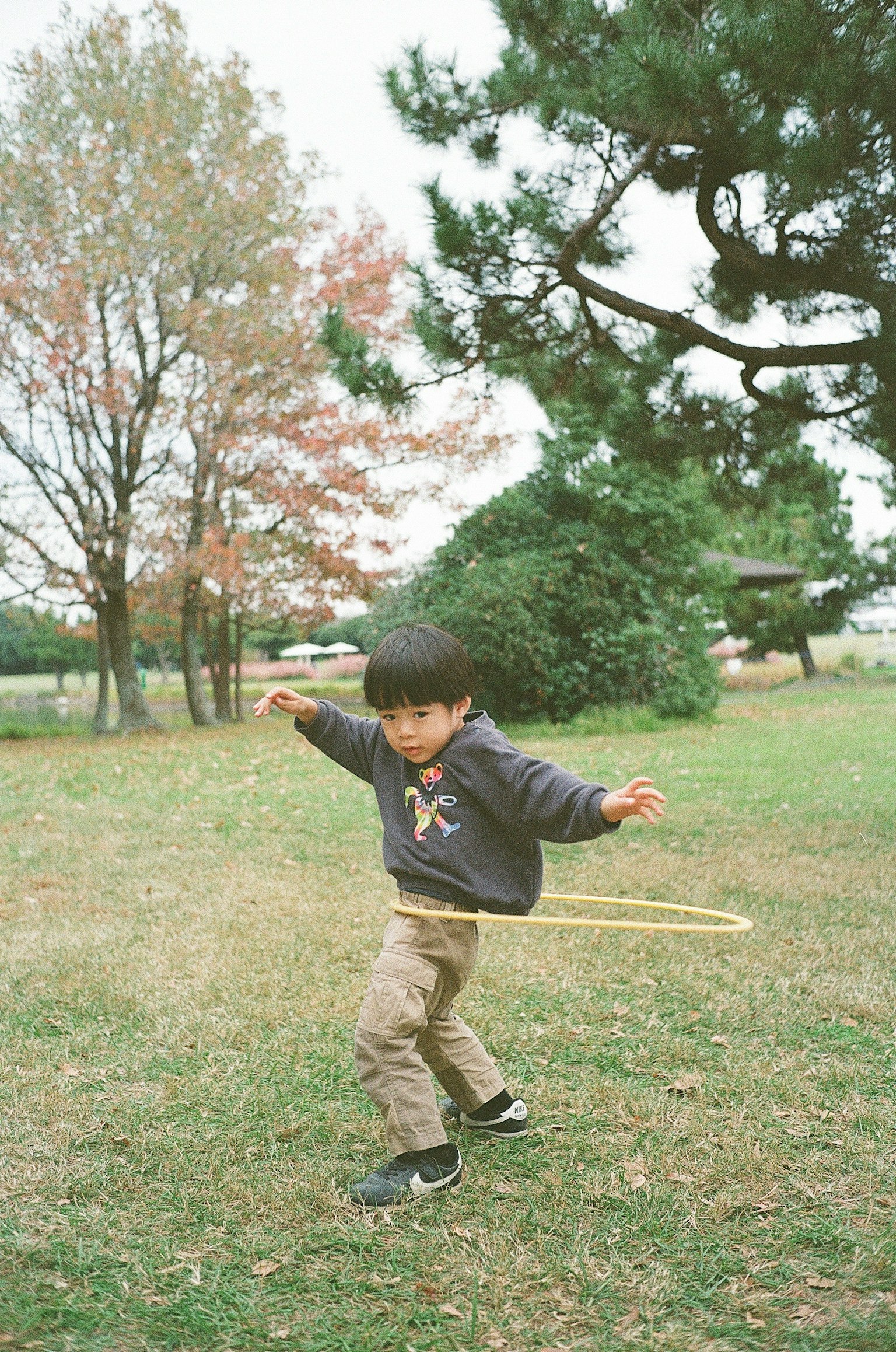 公園でフラフープを回している子供の写真 落ち葉のある背景と緑の木々