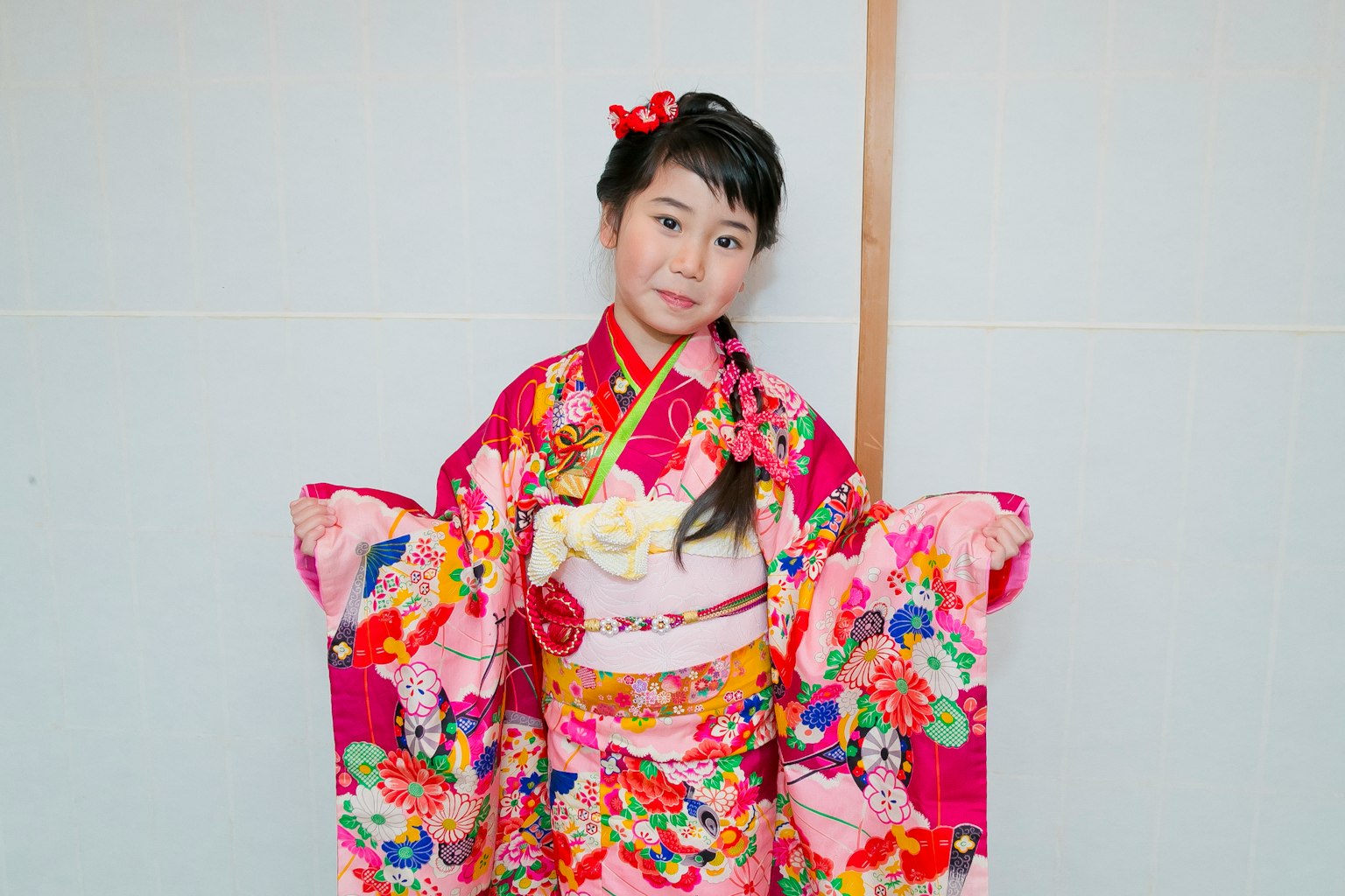 Gadis dalam kimono pink cerah tersenyum dalam pose tradisional