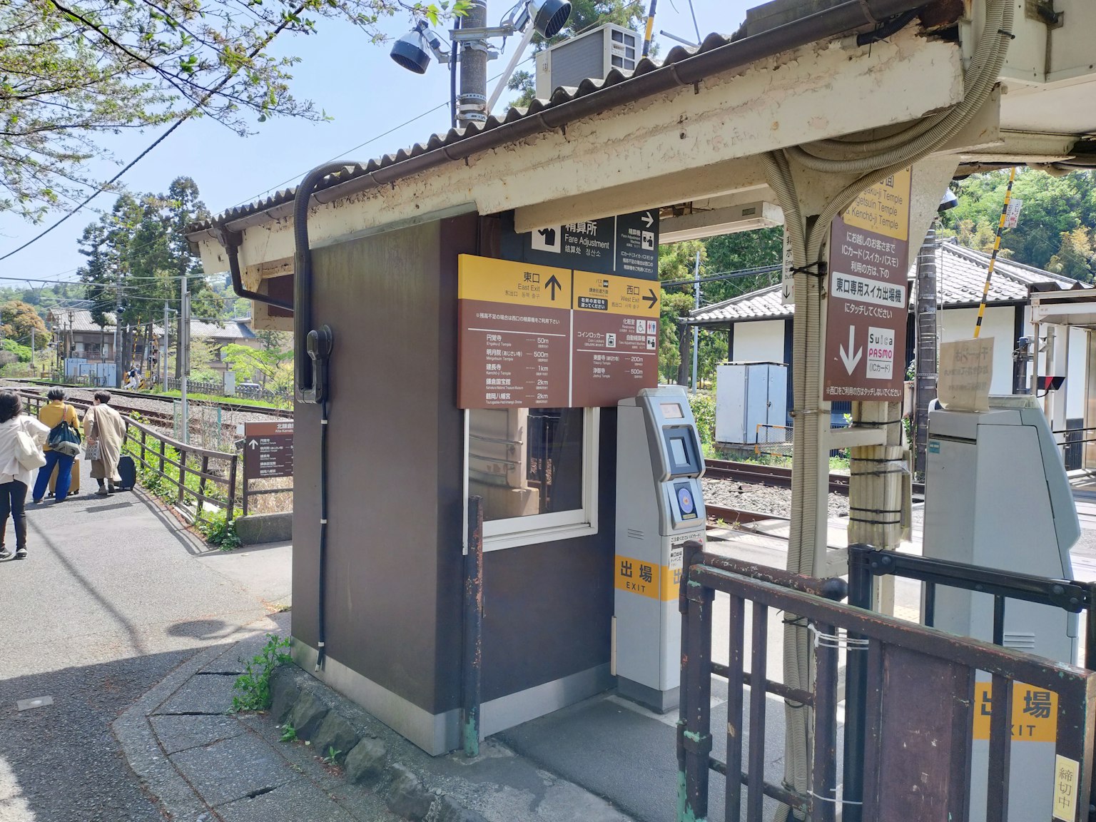 Loket tiket stasiun dengan papan nama dan pejalan kaki di dekatnya