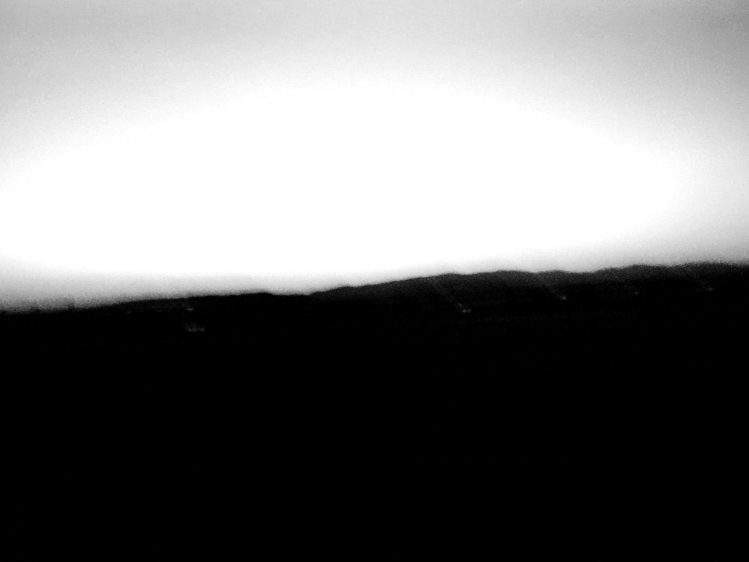 Schwarzweiß-Landschaftsfoto mit einem hellen Horizont, der sich von einem dunklen Terrain abhebt