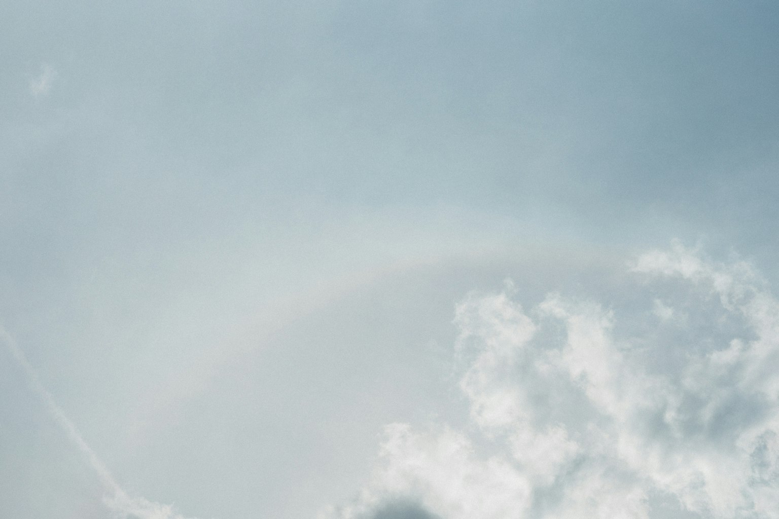 Pelangi lembut melengkung di langit biru muda dengan awan