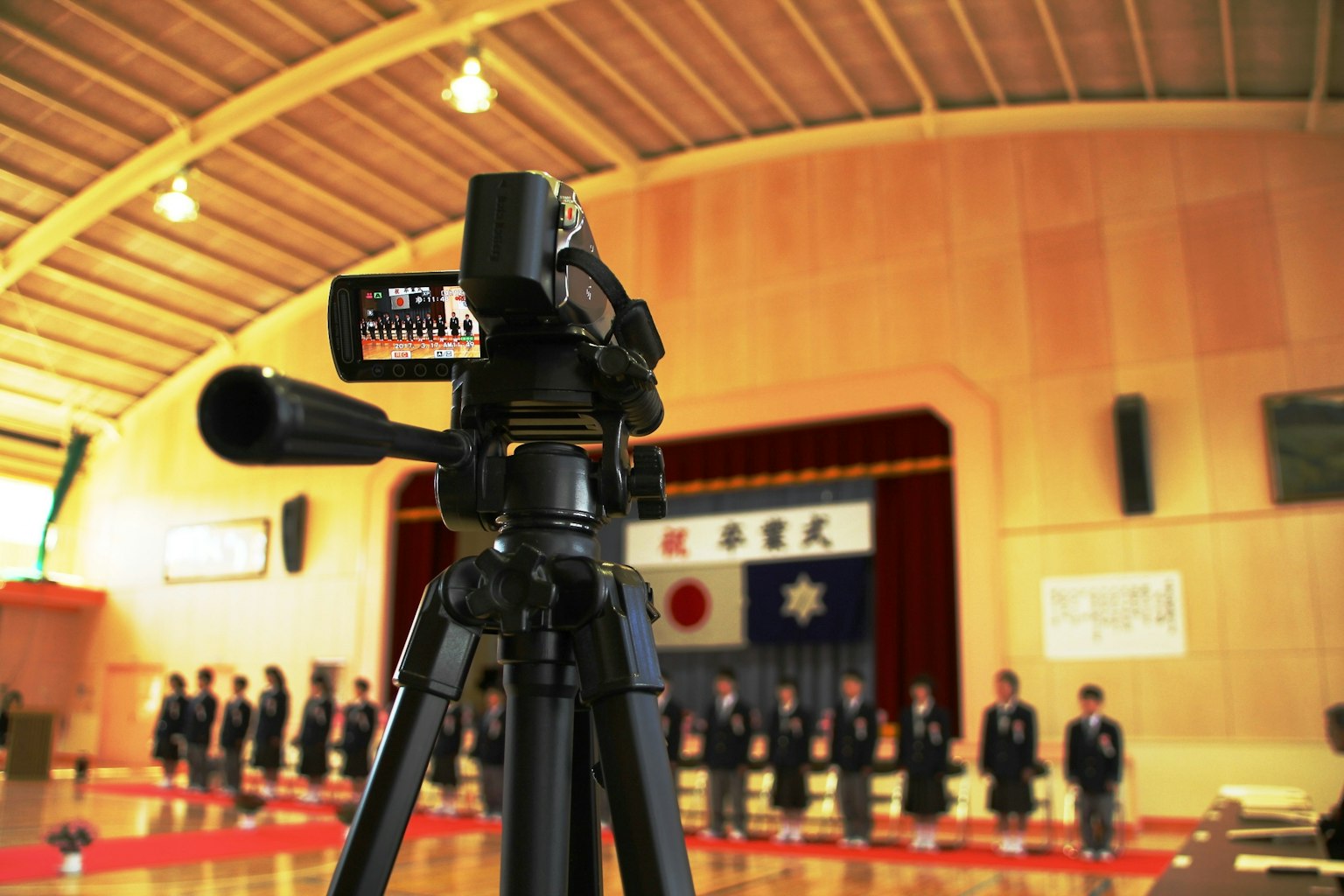 三脚上的相机对着有日本国旗的礼堂