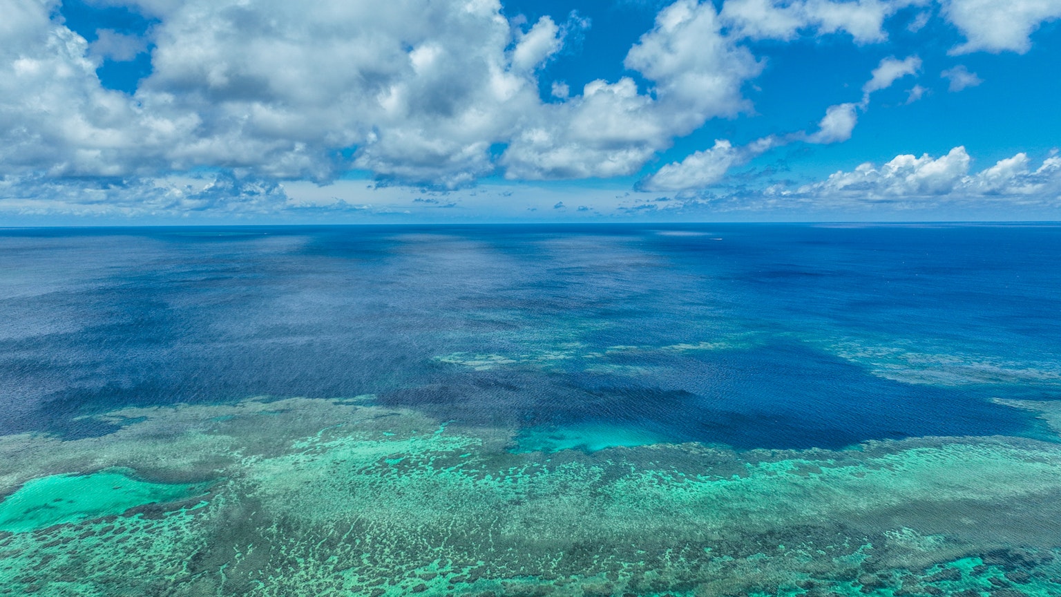 Luftaufnahme eines lebhaften blauen Ozeans mit Korallenriffen und verstreuten Wolken