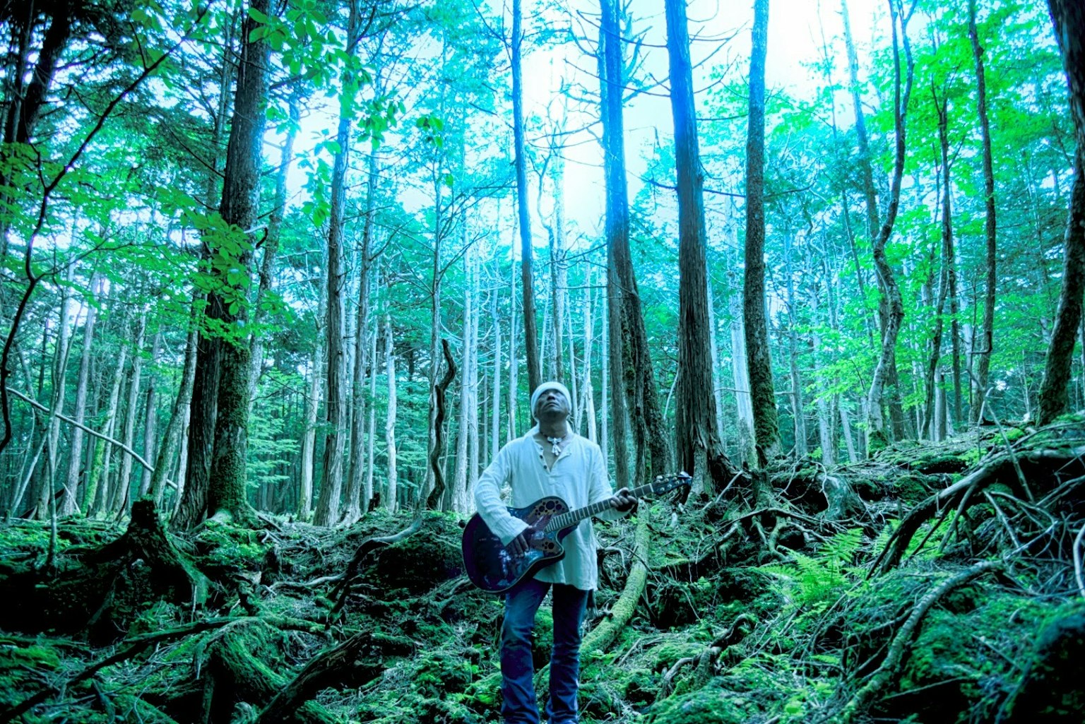 A person holding a guitar in a forest setting