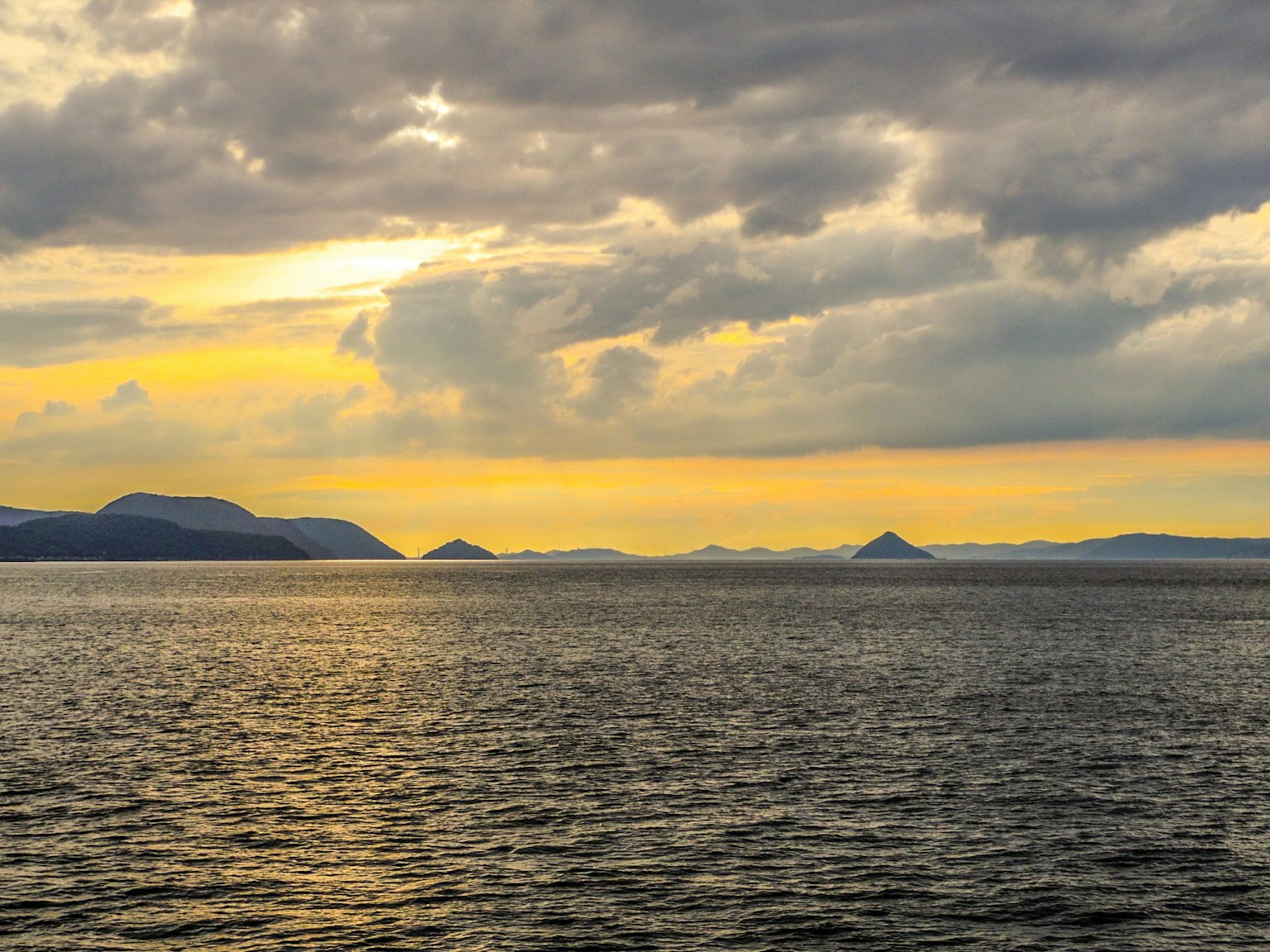 Paesaggio di oceano e isole che riflettono nuvole al tramonto e luce dorata