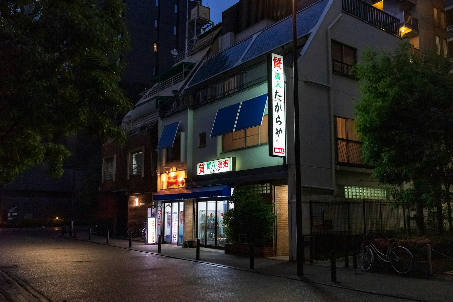 Esterno di un ristorante in città di notte con tende blu e insegne luminose