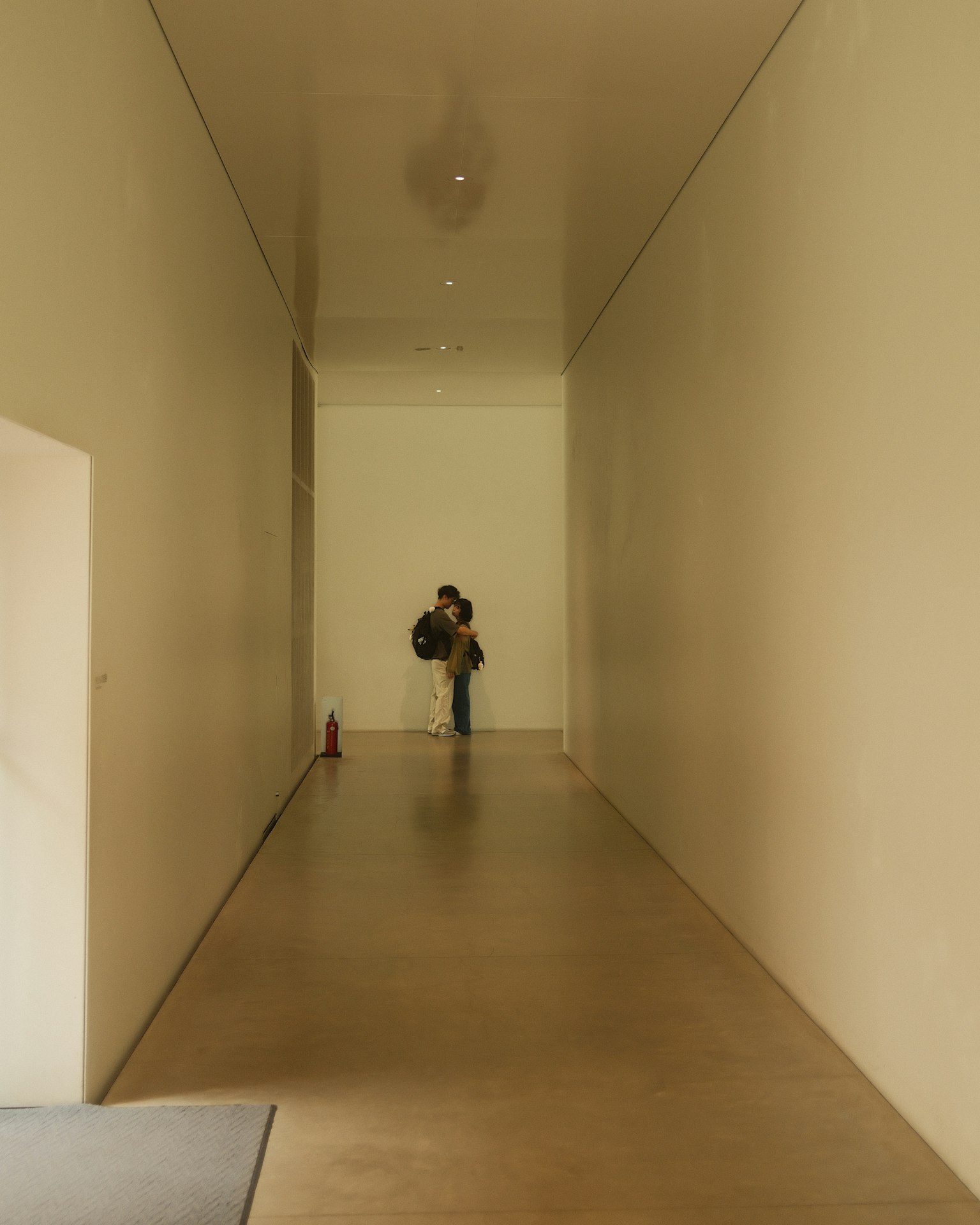 白い壁に囲まれた長い廊下に立つ人物のシルエット