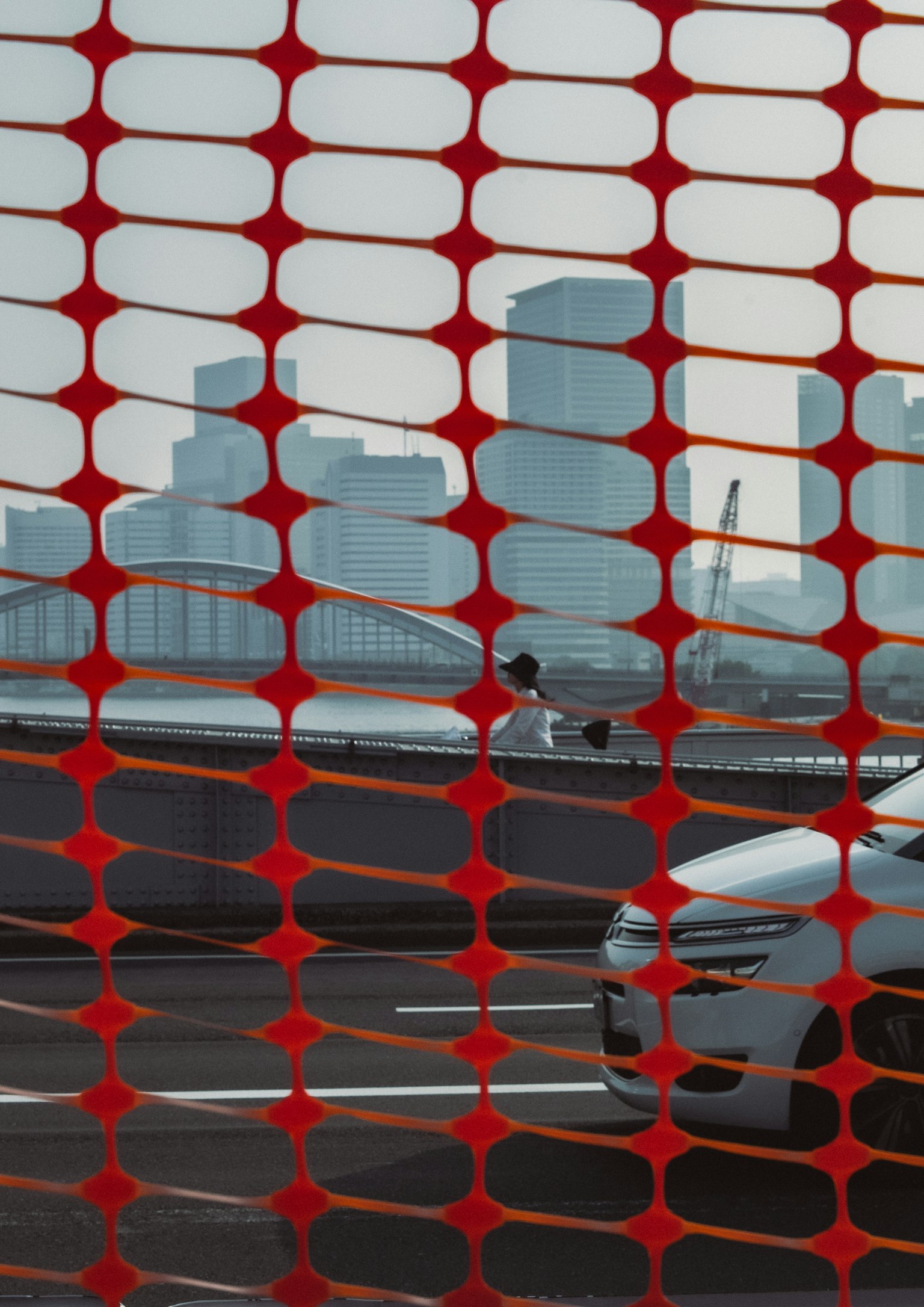 通过红色网状屏障看到的城市天际线和前景中的汽车