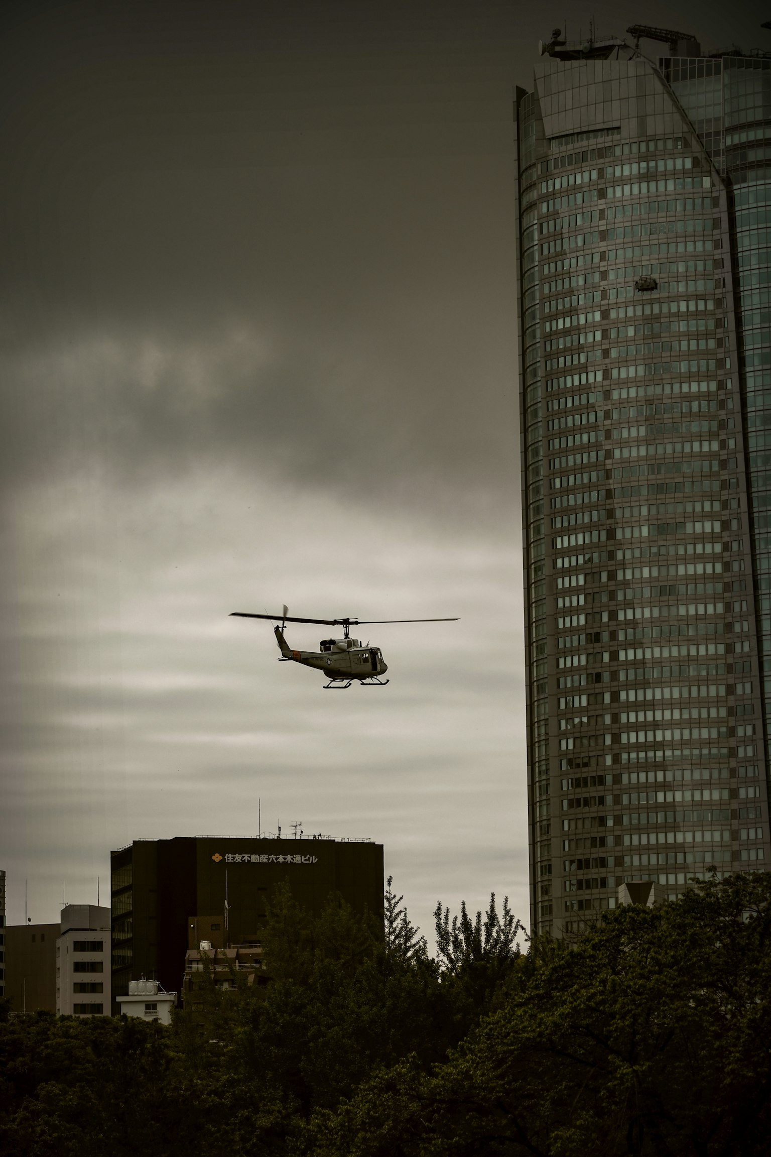Helicopter flying near a skyscraper under a dark sky