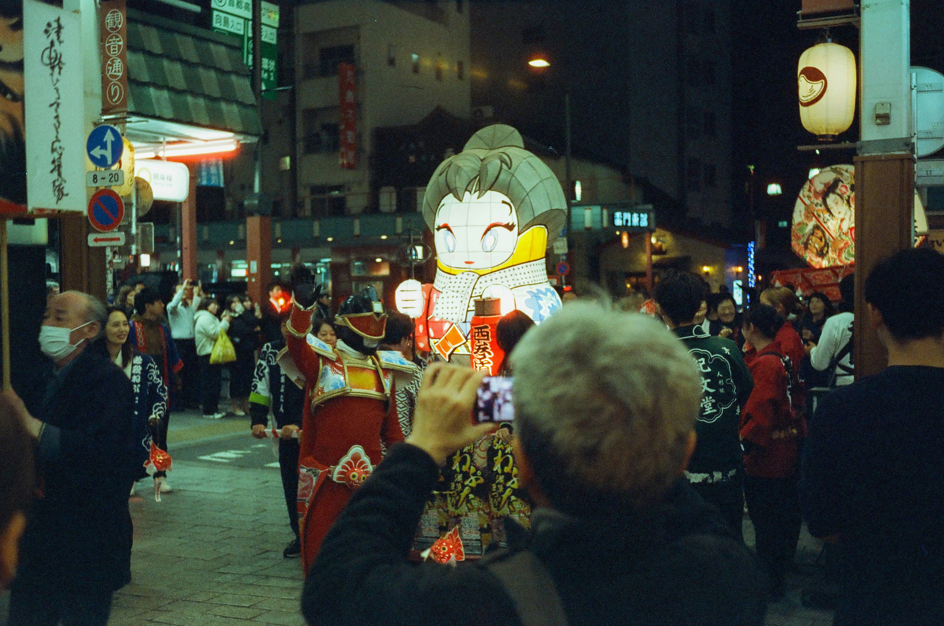夜の商店街で提灯と着ぐるみのキャラクターが並ぶ通り