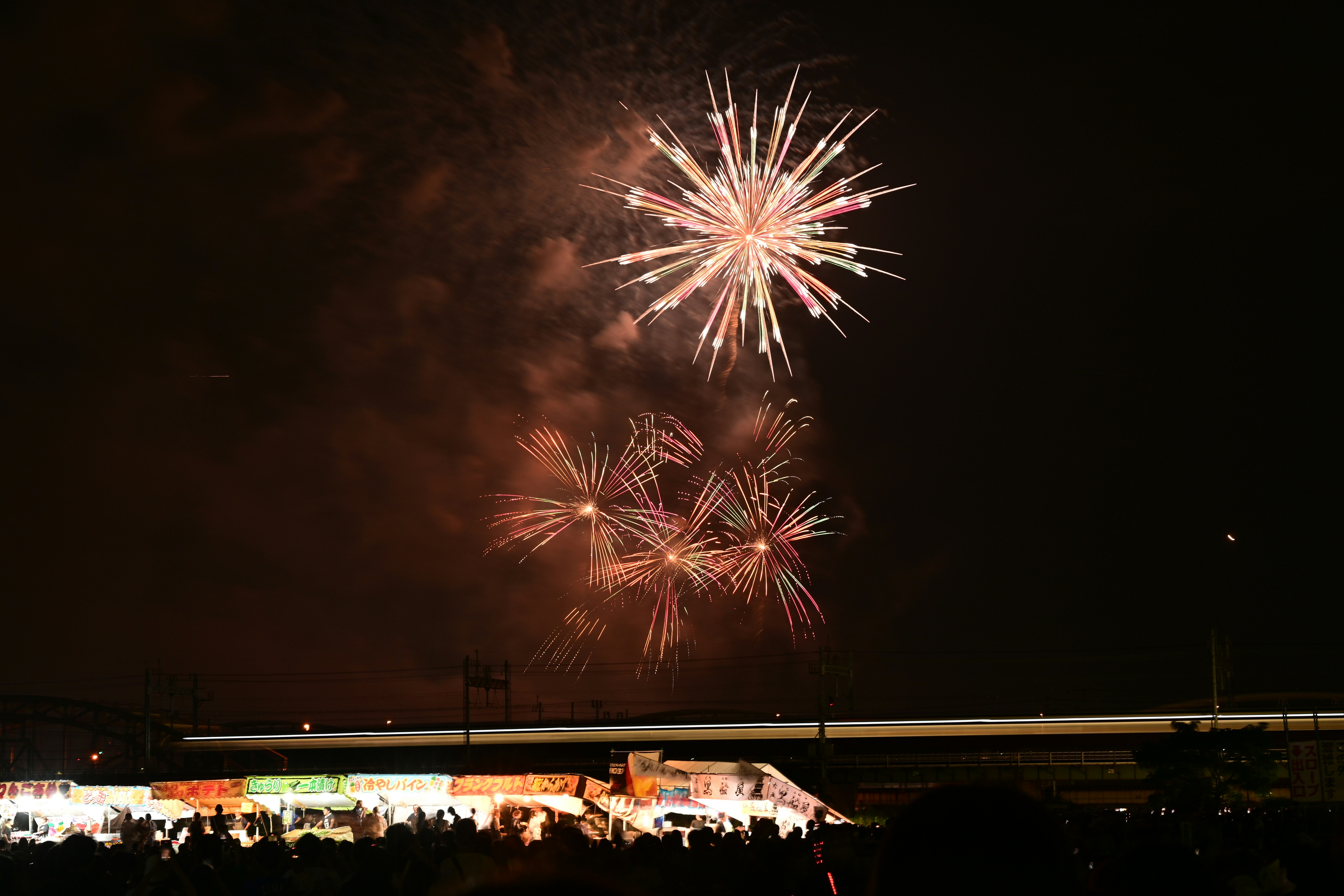 夜空に打ち上がる花火と屋台の並ぶ会場の風景