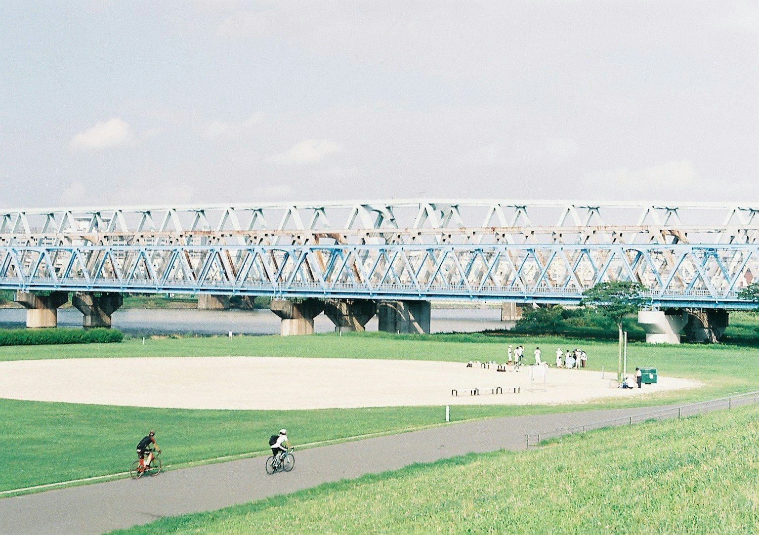 Des personnes faisant du vélo sous un pont bleu avec une pelouse verte spacieuse