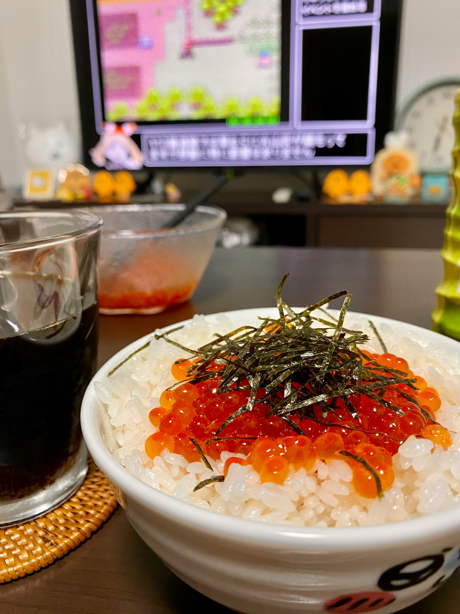 Bowl of rice topped with salmon roe and seaweed with a gaming screen in the background