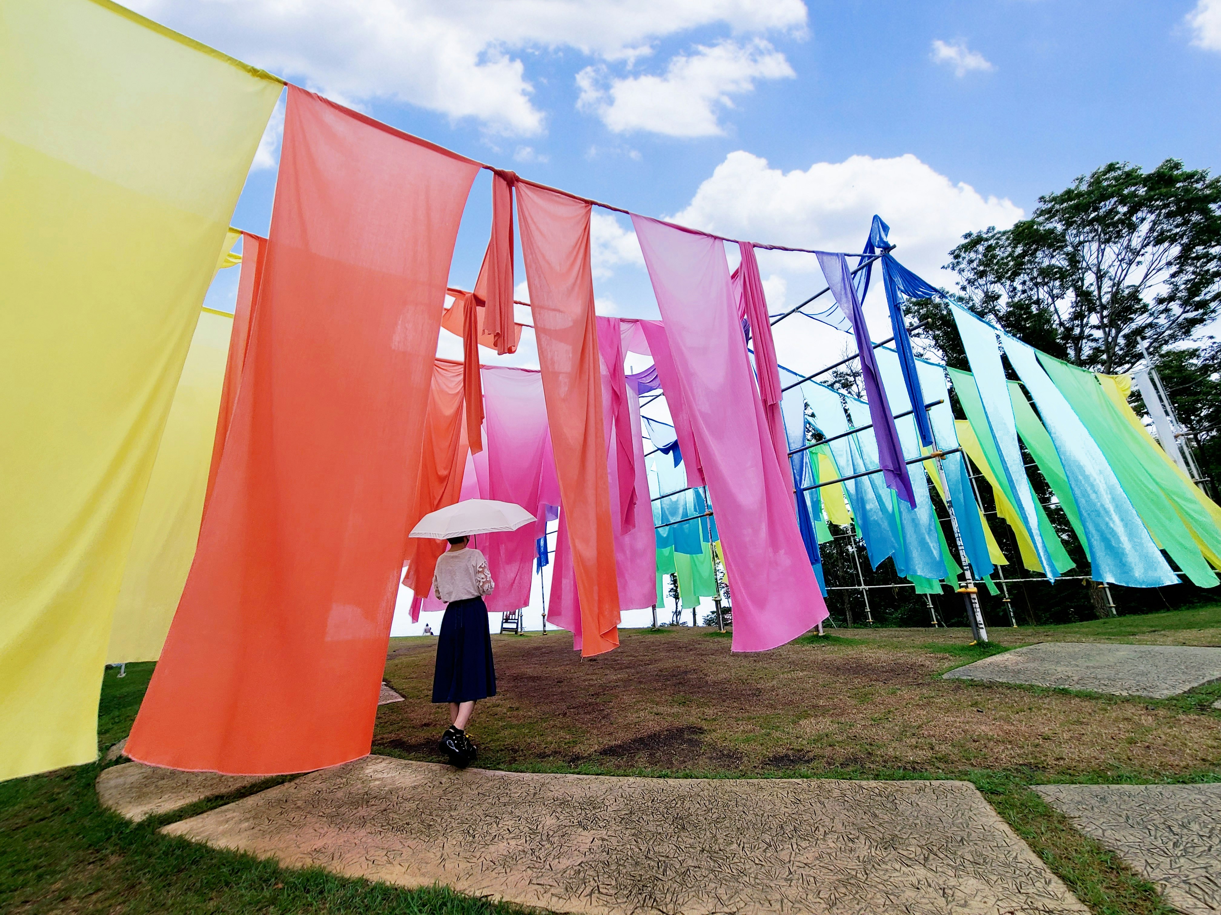 芝生の上に並ぶカラフルな布の旗とテントのある屋外イベント会場