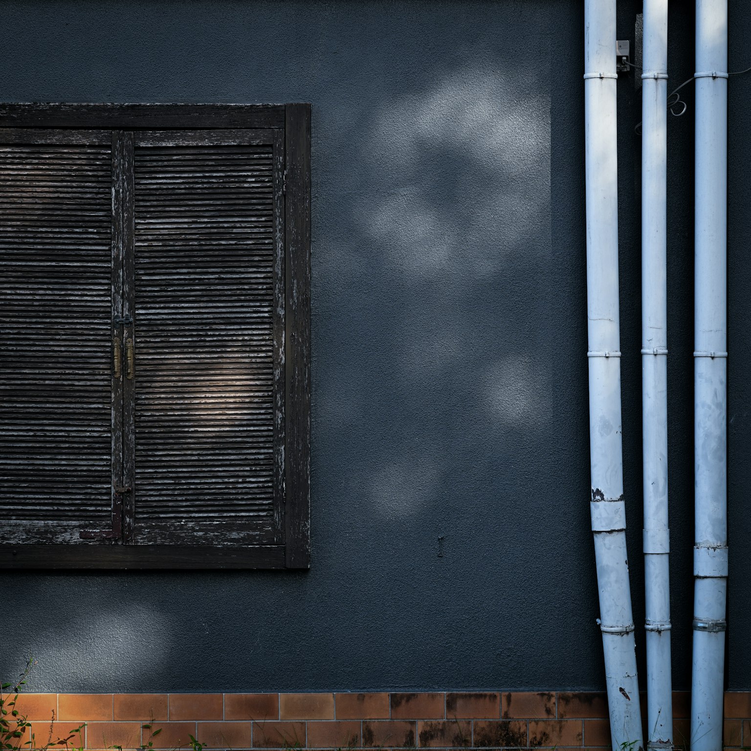 A simple composition featuring an old wooden shutter on a blue wall with white pipes