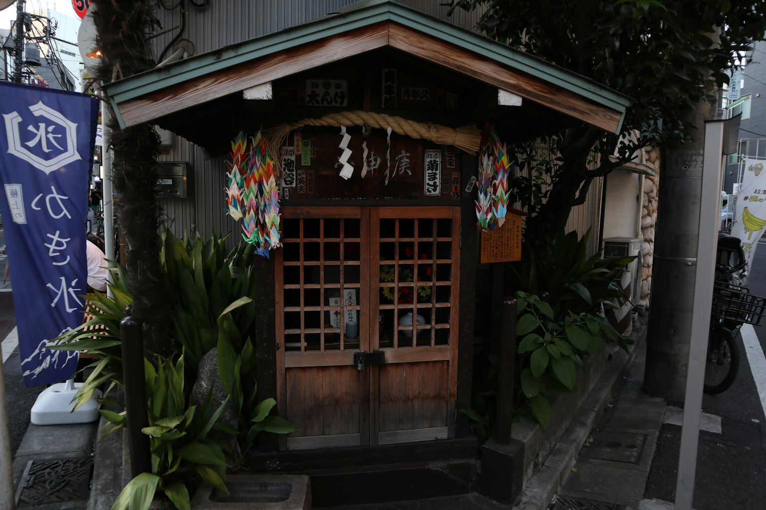 传统日本神社小屋，木制入口，周围环绕着郁郁葱葱的绿色植物和五彩缤纷的装饰