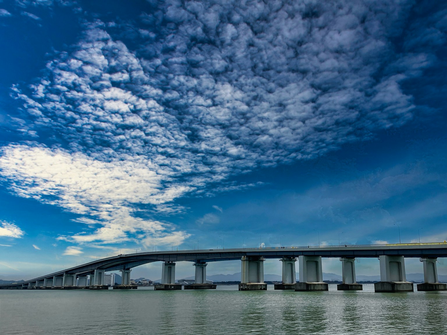 A scenic view of a bridge under a blue sky with white clouds