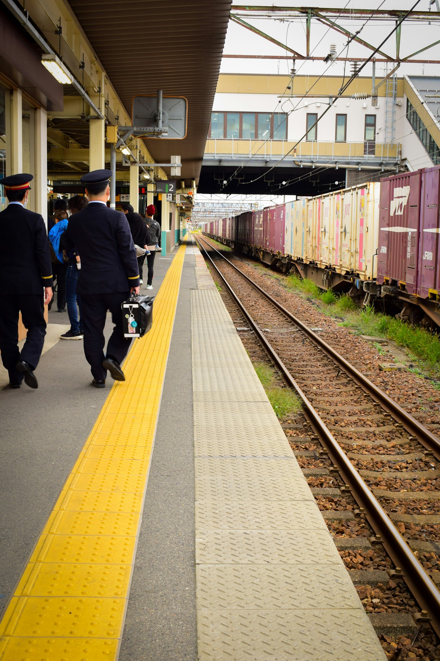 Szene mit zwei Bahnpersonal auf einem Bahnsteig mit Güterzug in Sicht