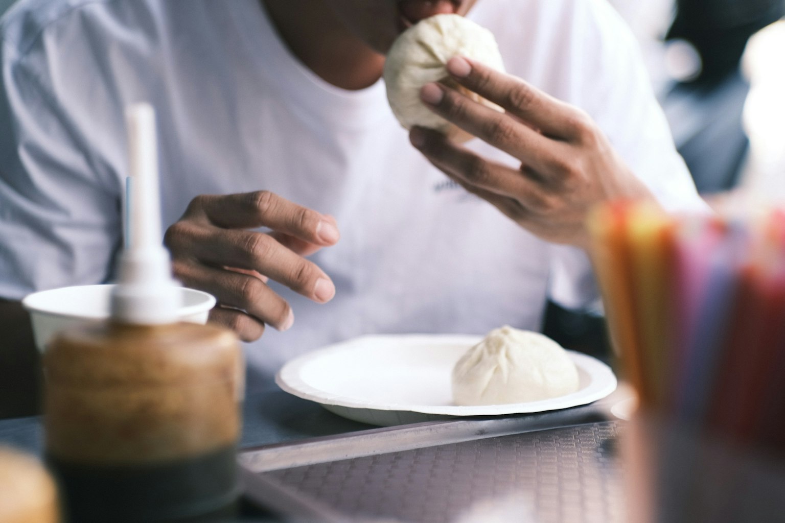 Un uomo che mangia un panino bianco con le mani che tiene il panino e un altro panino su un piatto