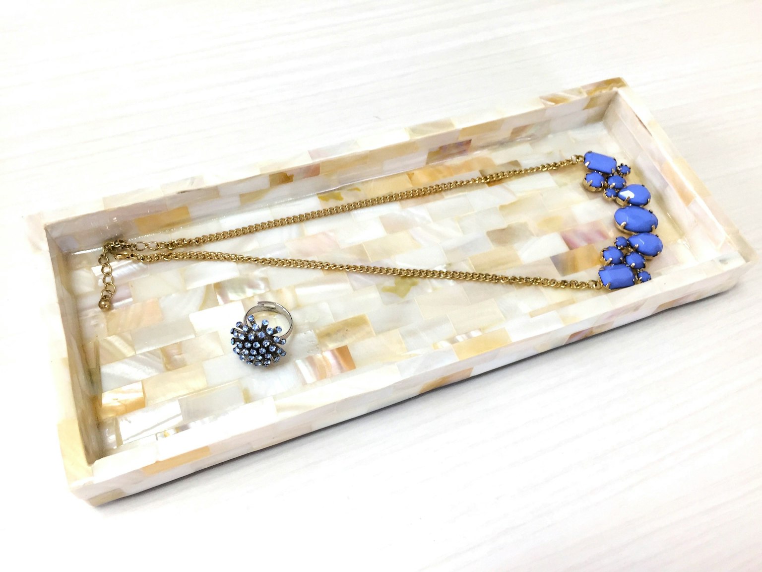 Collana in pietre preziose blu e anello esposti su un vassoio bianco