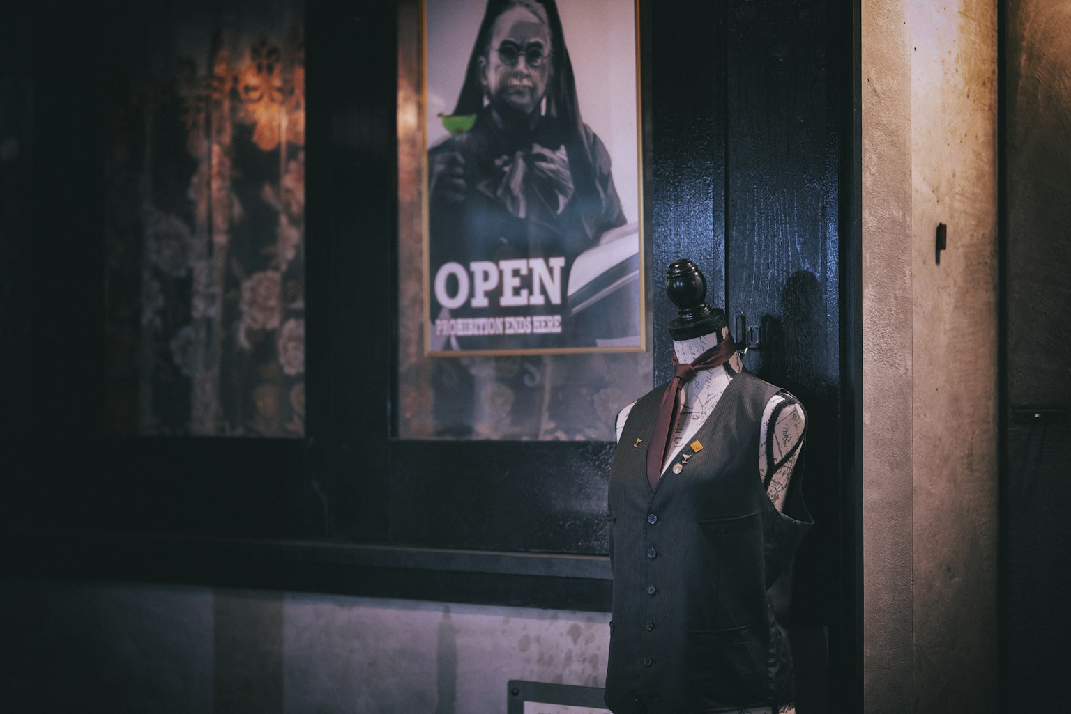 A mannequin dressed in a suit next to an open sign in a shop window