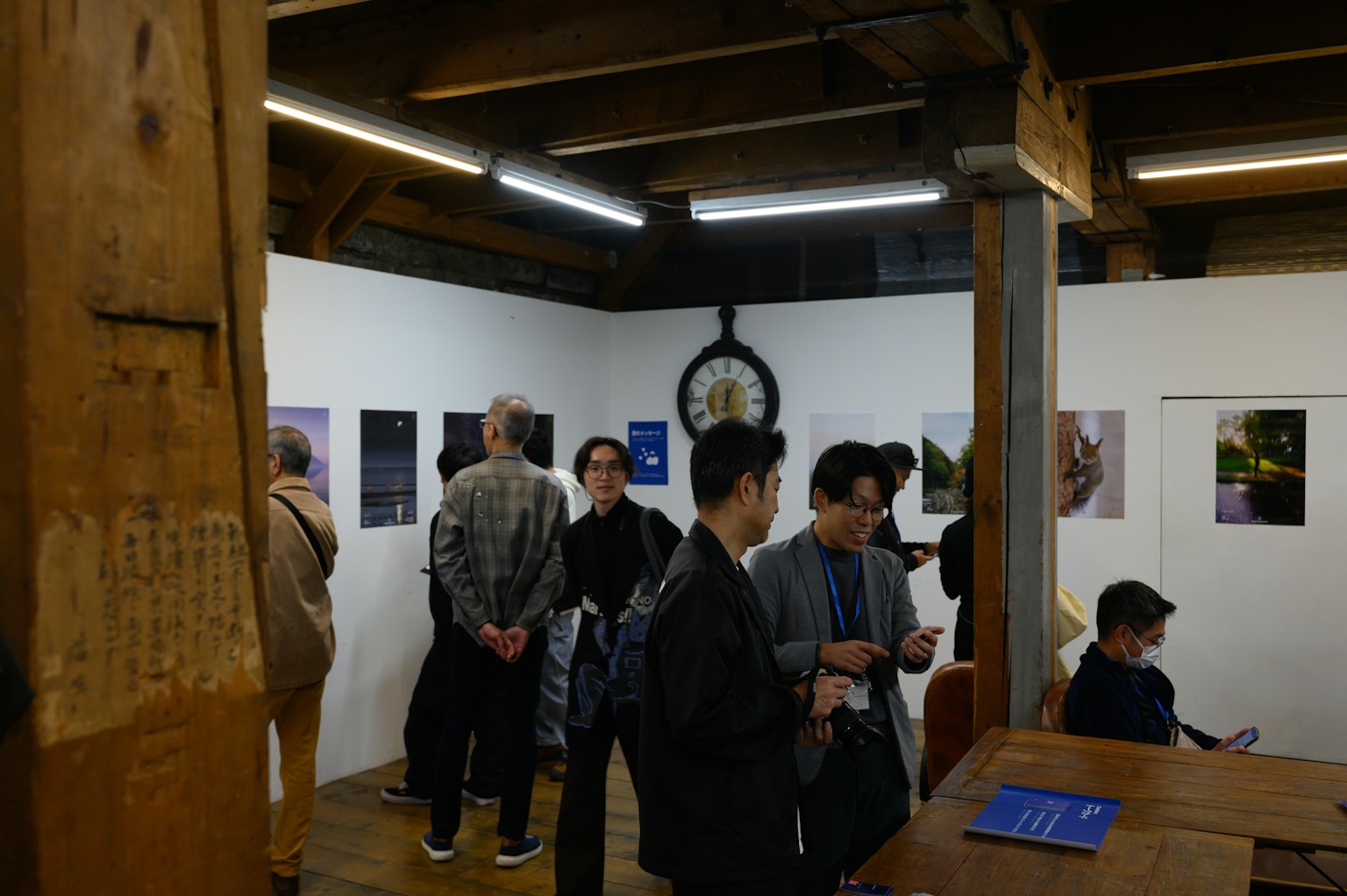 People viewing photographs in an art gallery with a clock on the wall