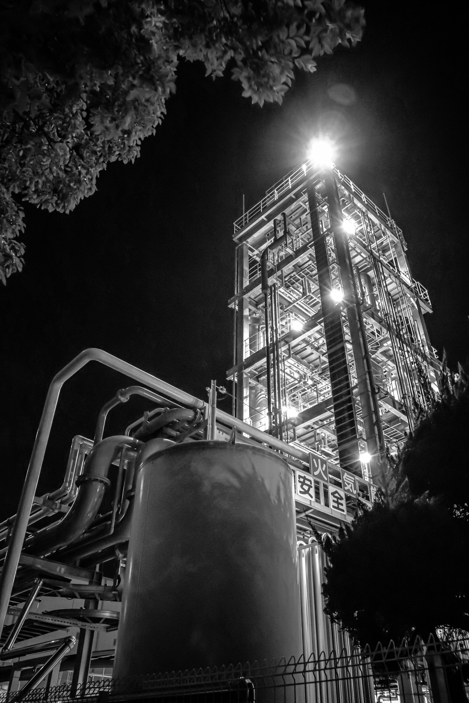 Black and white image of an industrial facility tower and pipes at night