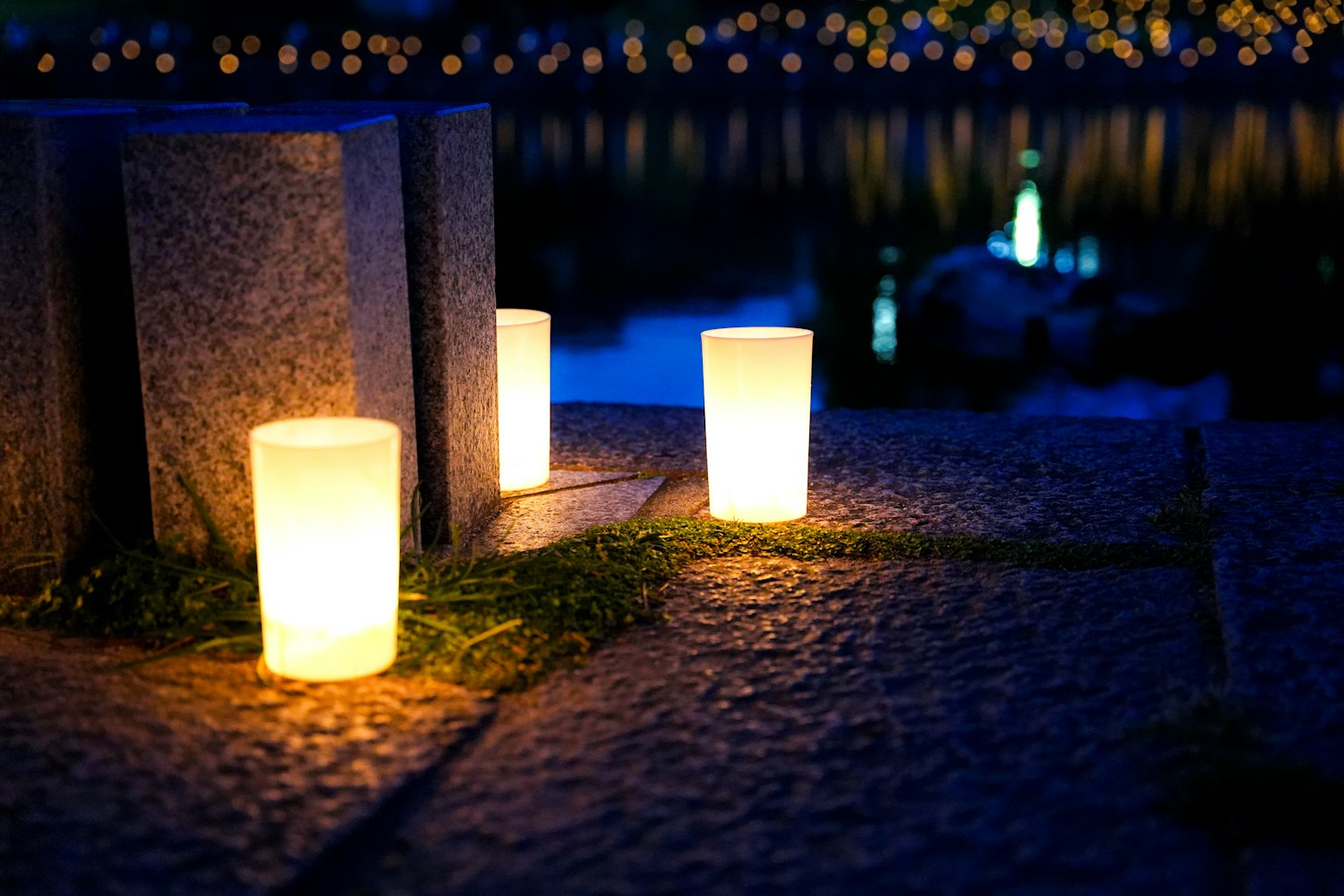 Helle Kerzen auf einem Steinpflaster am See bei Nacht