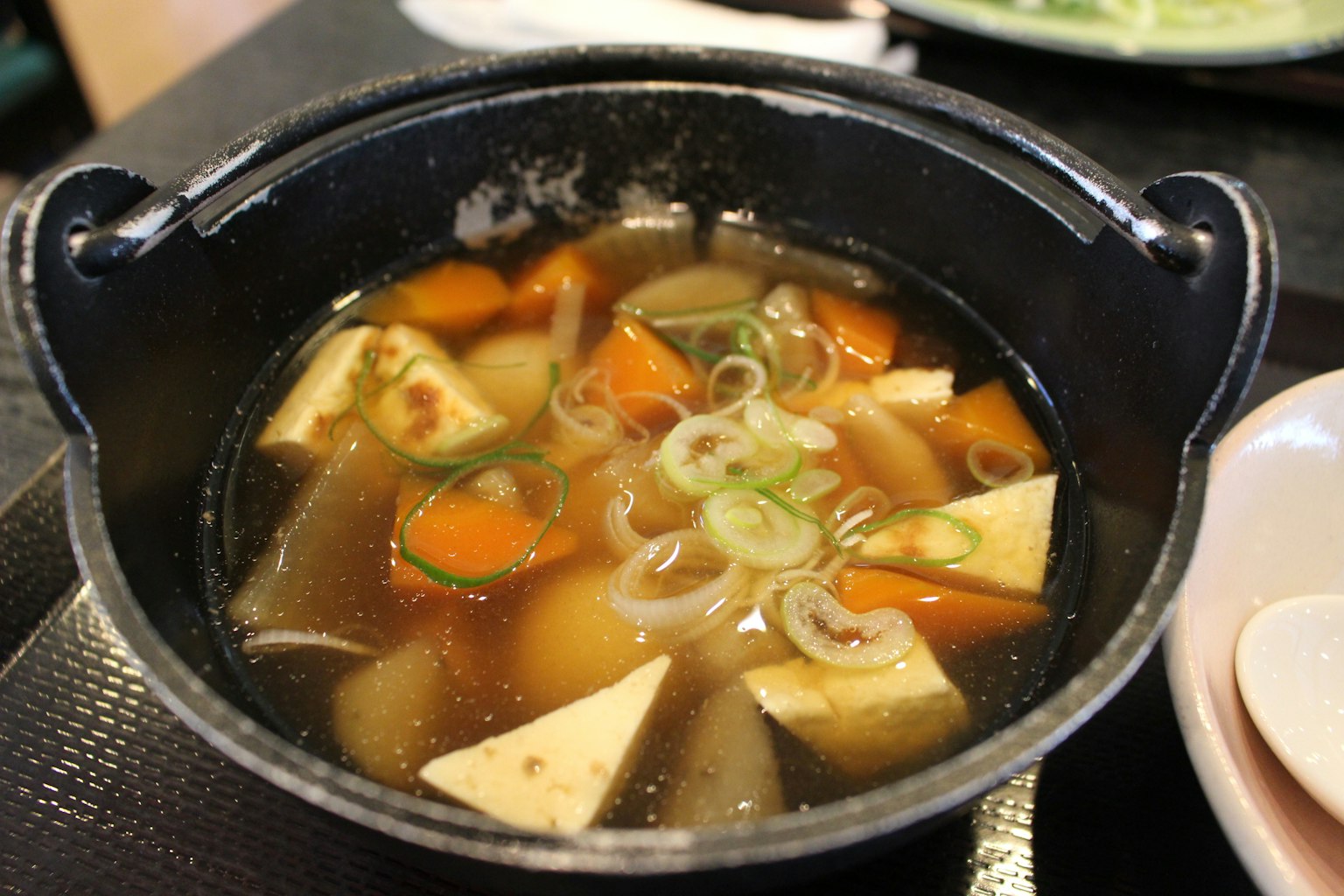 검은 냄비에 담긴 푸짐한 수프 두부와 다양한 채소가 보인다