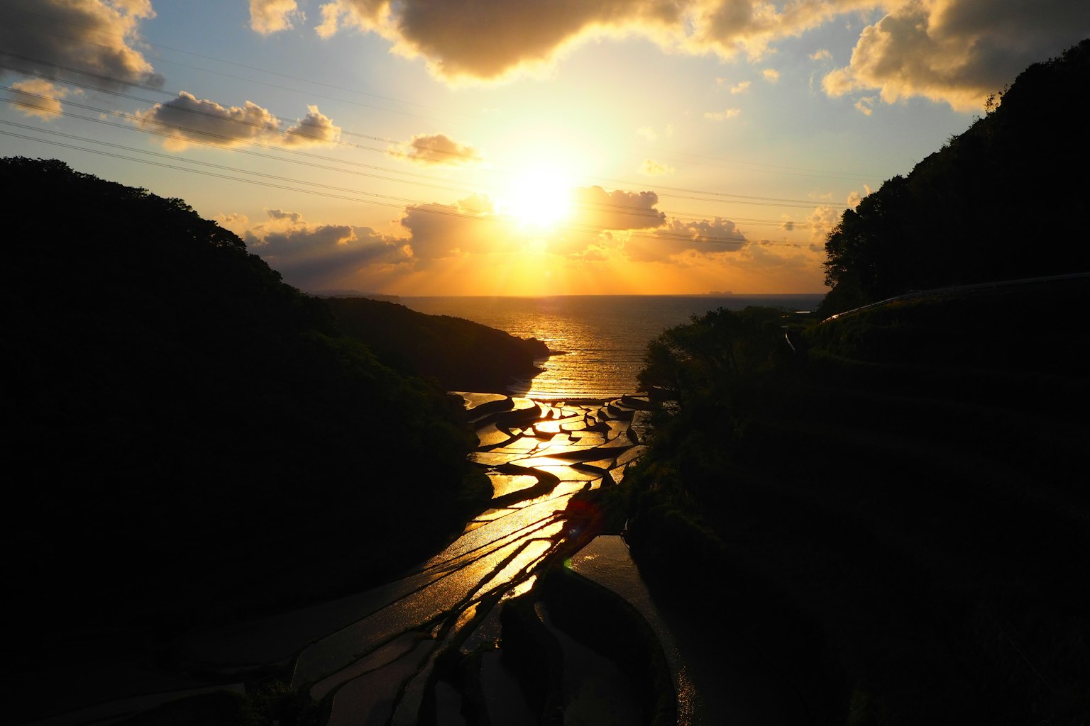 Impresionante paisaje de un atardecer sobre el océano con siluetas de colinas verdes