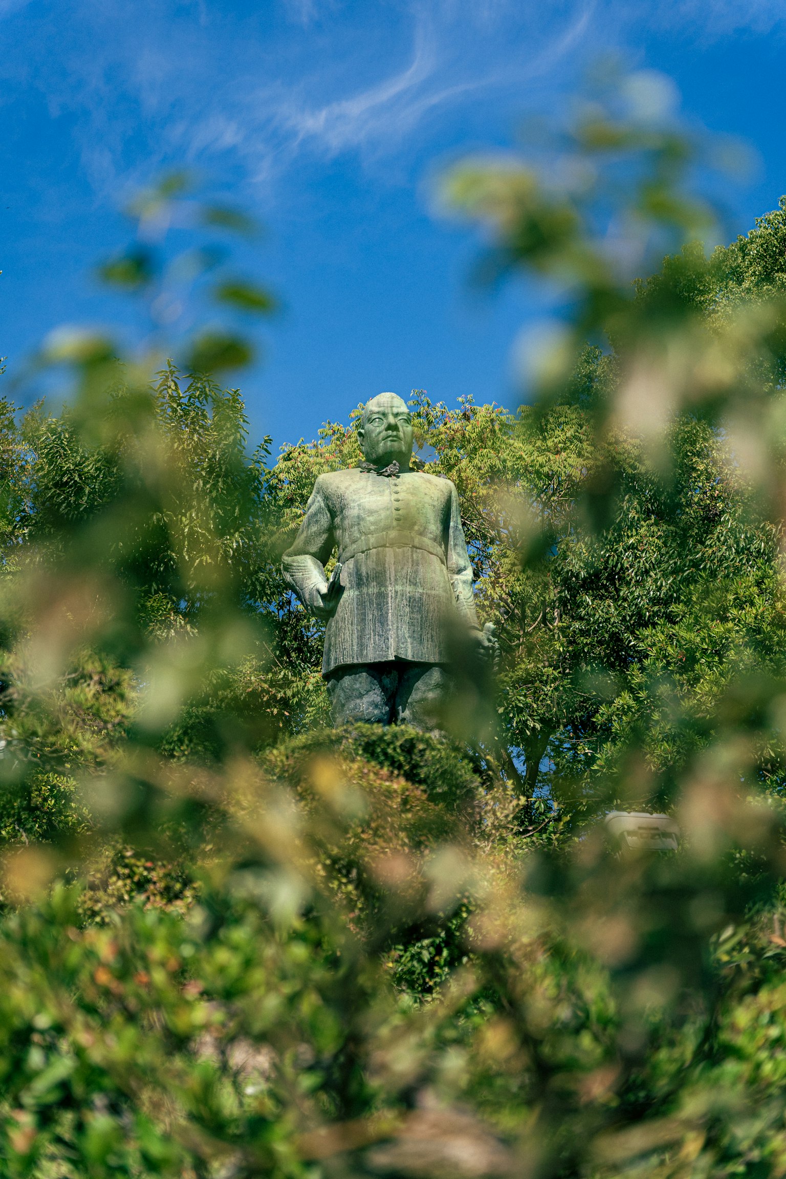 Gran estatua visible a través del follaje verde bajo un cielo azul