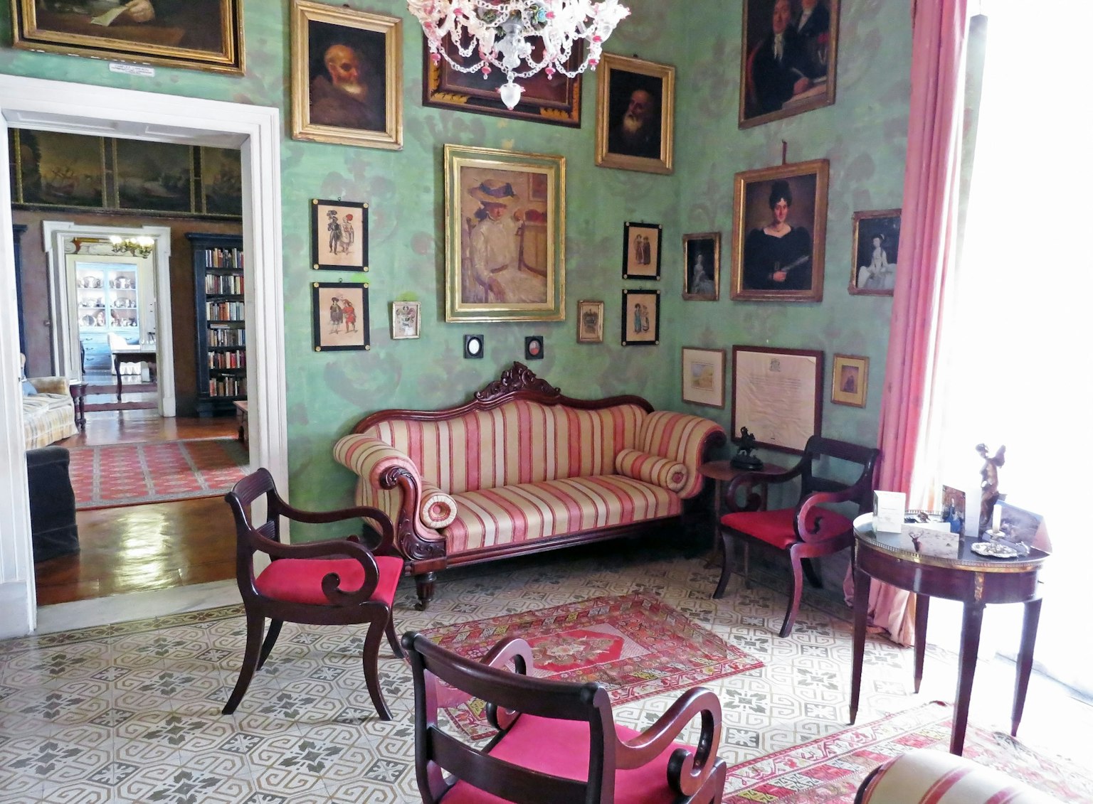 Klassisches Wohnzimmer mit grünen Wänden, rotem Streifensofa und verschiedenen Gemälden