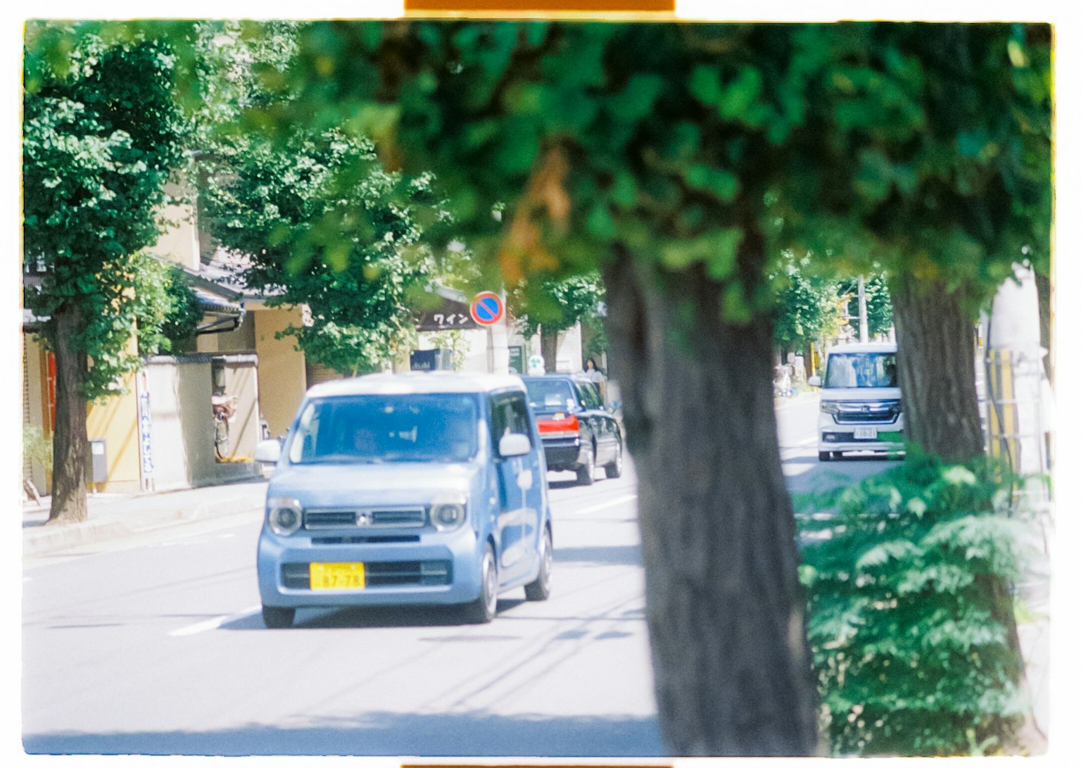 Ein blauer Wagen fährt eine ruhige Straße entlang, gesäumt von grünen Bäumen