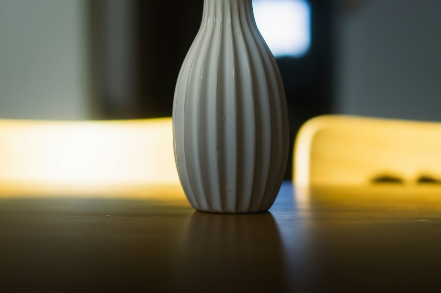 Un vaso bianco a strisce posato su un tavolo con una luce gialla soffusa sullo sfondo