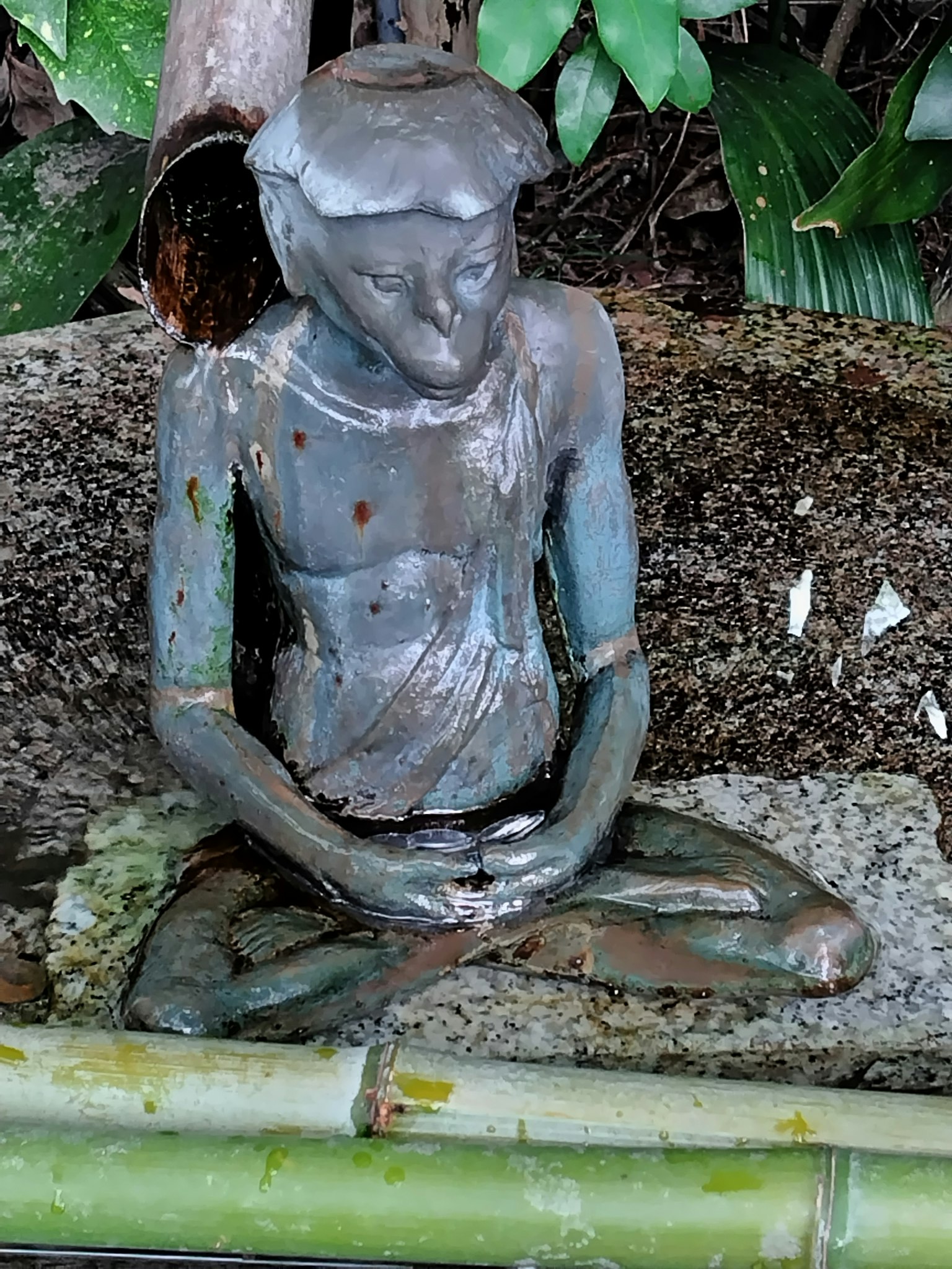 Estatua de bronce sentada rodeada de plantas verdes