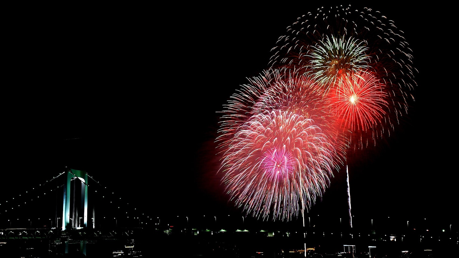 Des feux d'artifice éclatent dans le ciel nocturne avec le pont Rainbow en arrière-plan