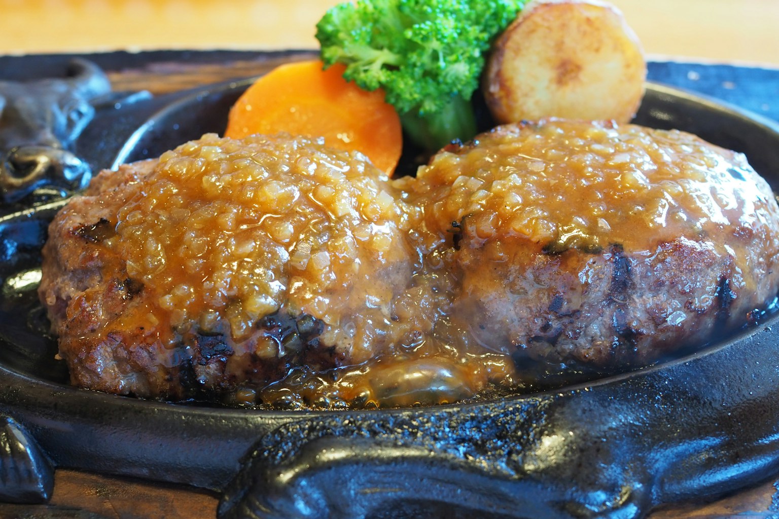 Zischende Hamburger-Patties mit Sauce auf einem heißen Teller serviert mit Gemüse